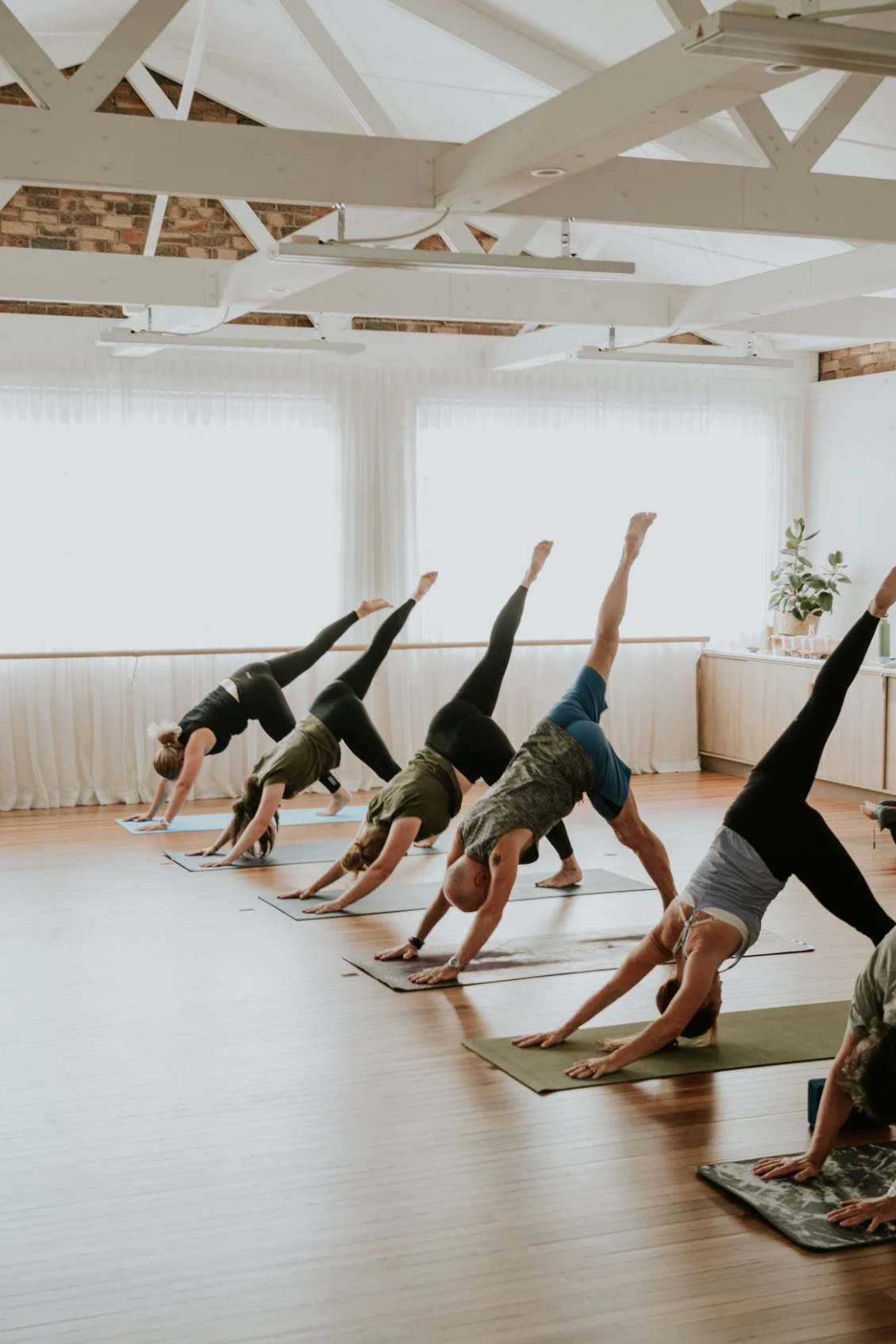 Group of people doing yoga in a bright studio, performing downward dog pose on mats.