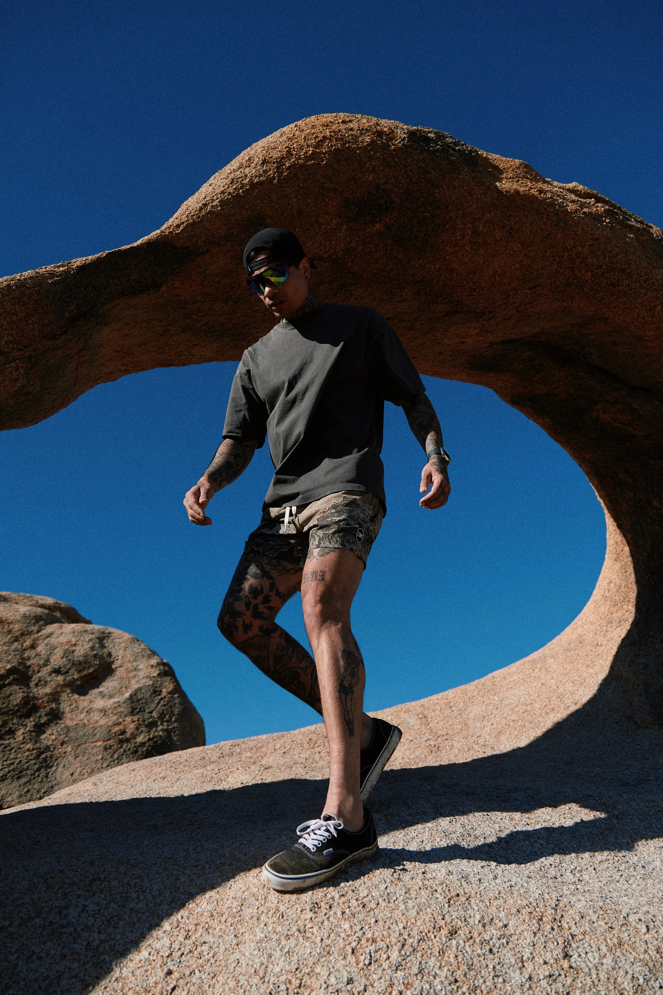 Activewear photography in Los Angeles: camo shorts, walking under a rock arch in the Alabama Hills, by Moises Martinez