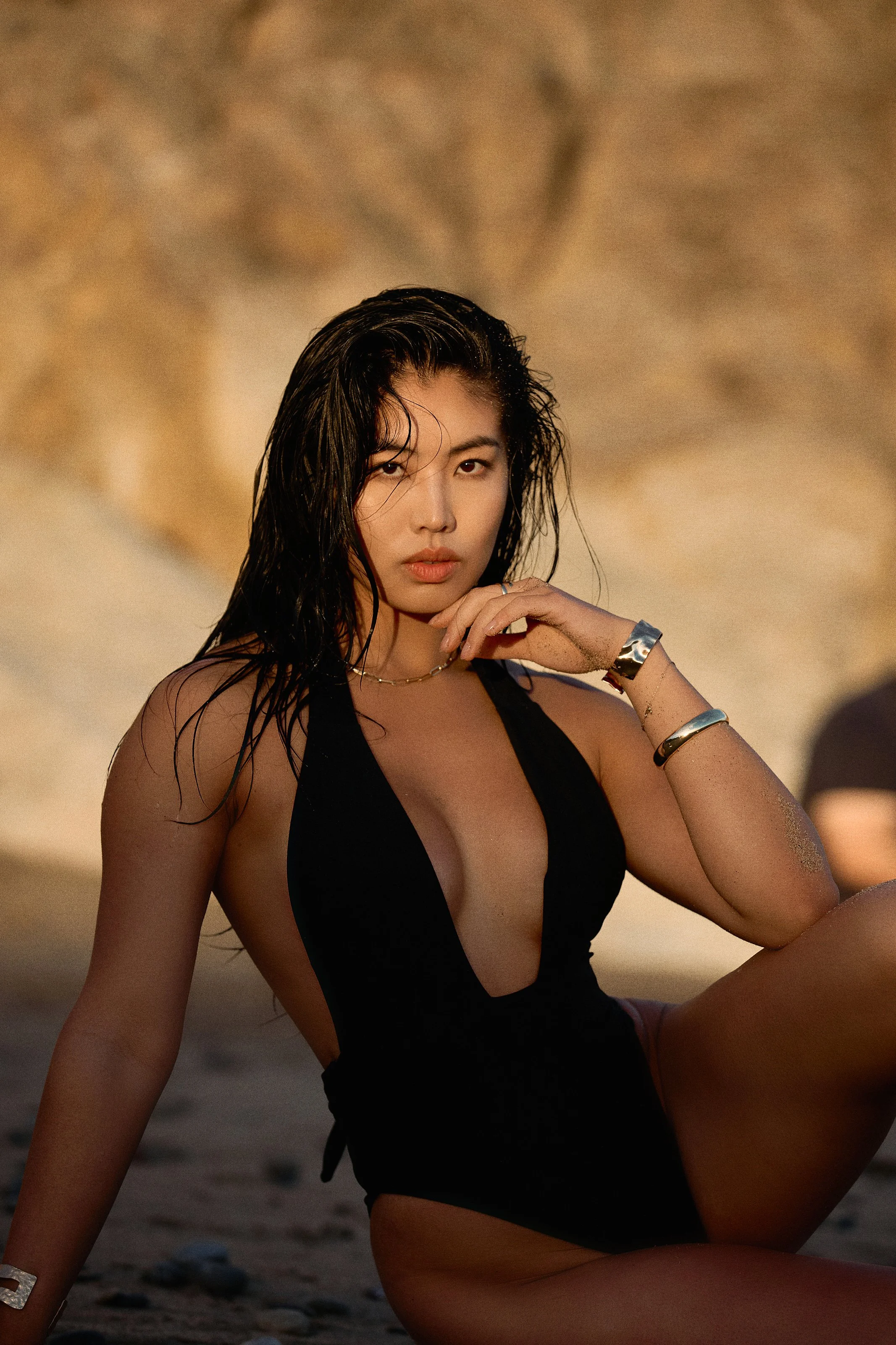 A woman in a black swimsuit sitting on the beach.