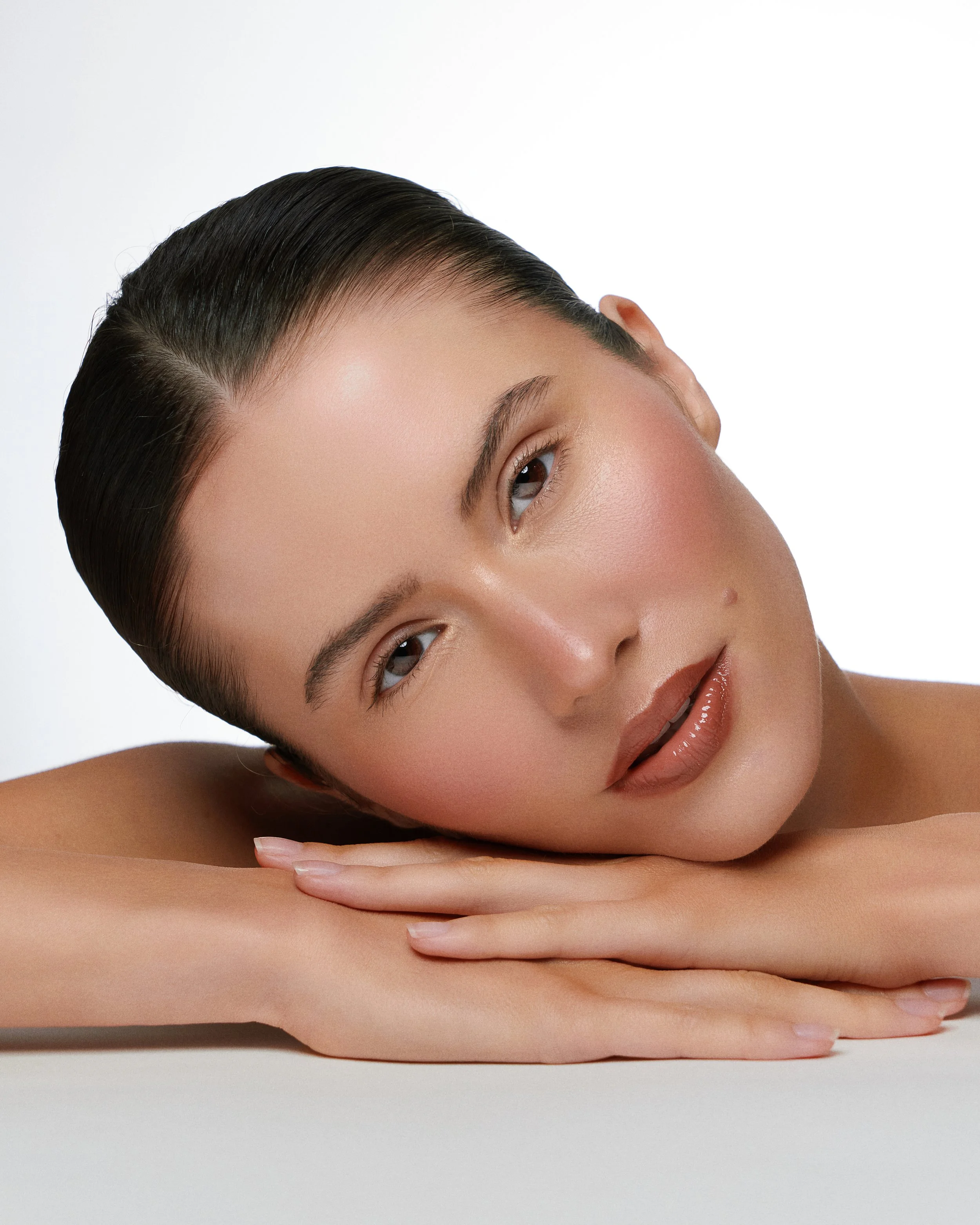 Beauty photography in Los Angeles: head resting on hands, glowing skin on white, by Moises Martinez
