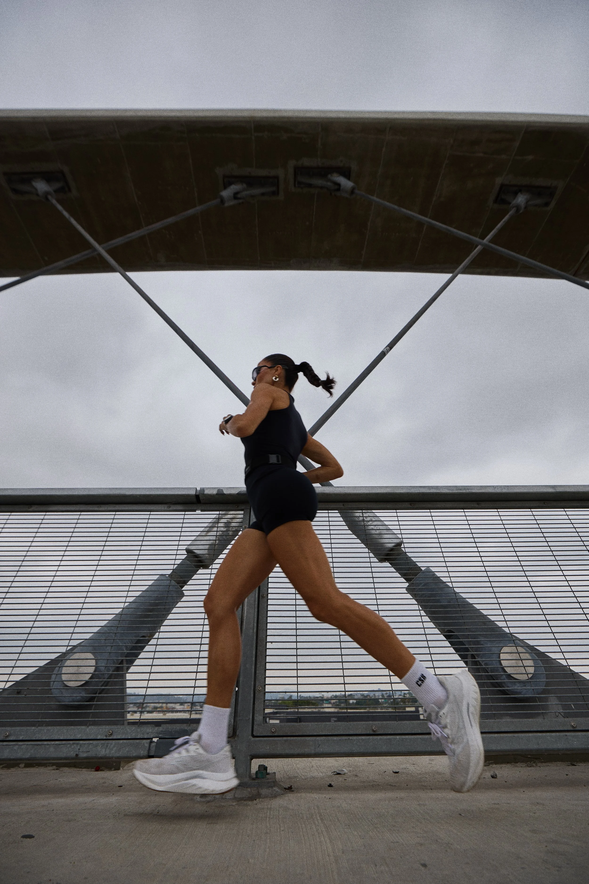 A woman running on a bridge under a large bridge structure on a cloudy day.