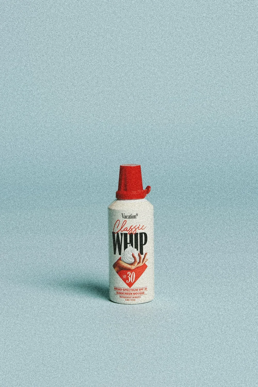 A bottle of Vacation Classic Whip sunscreen mousse with SPF 30 against a plain blue background.