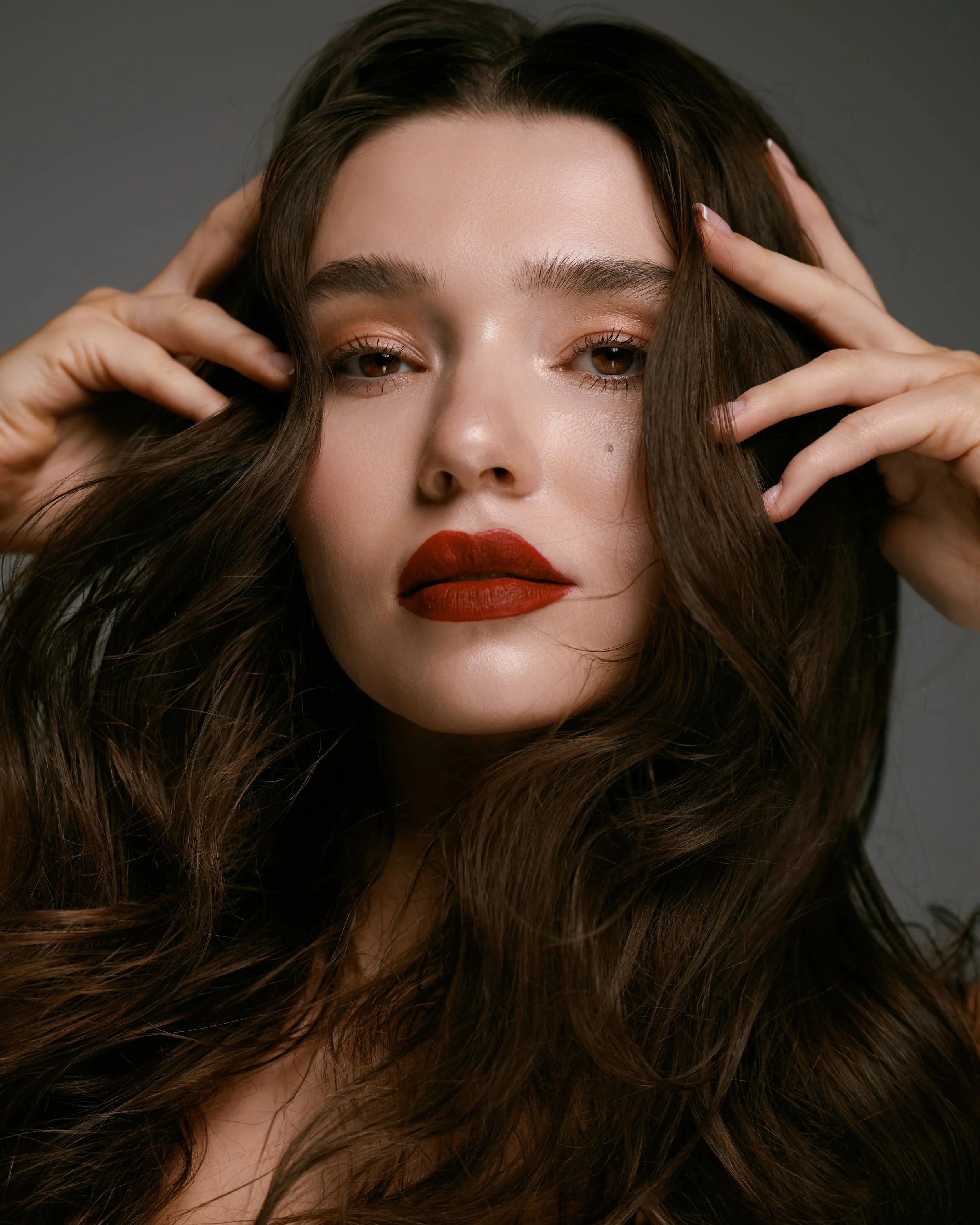 Beauty photography in Los Angeles: red lip with hands in hair on a dark backdrop, by Moises Martinez