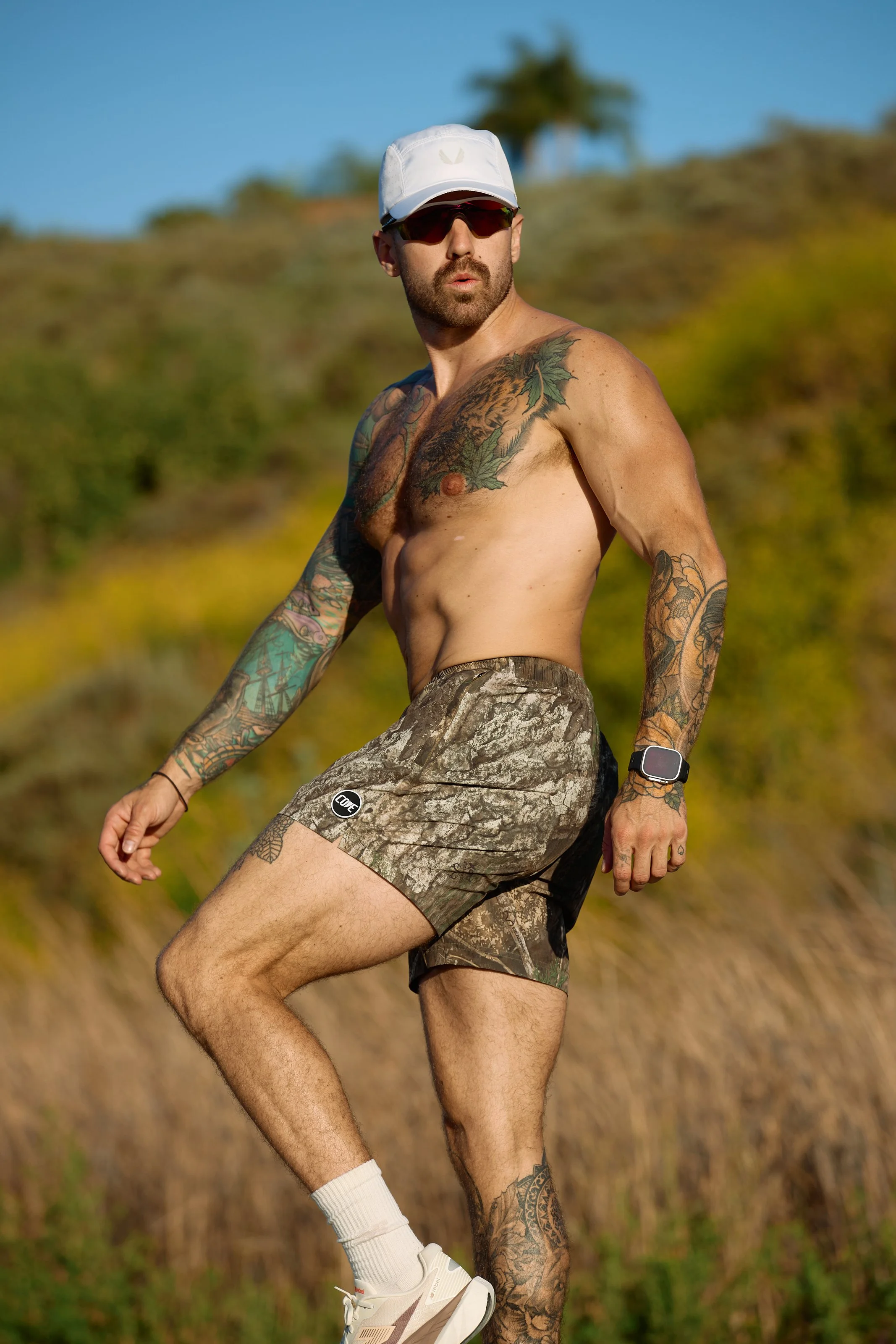Activewear photography in Los Angeles: trail runner in camo shorts and cap on a hillside, by Moises Martinez