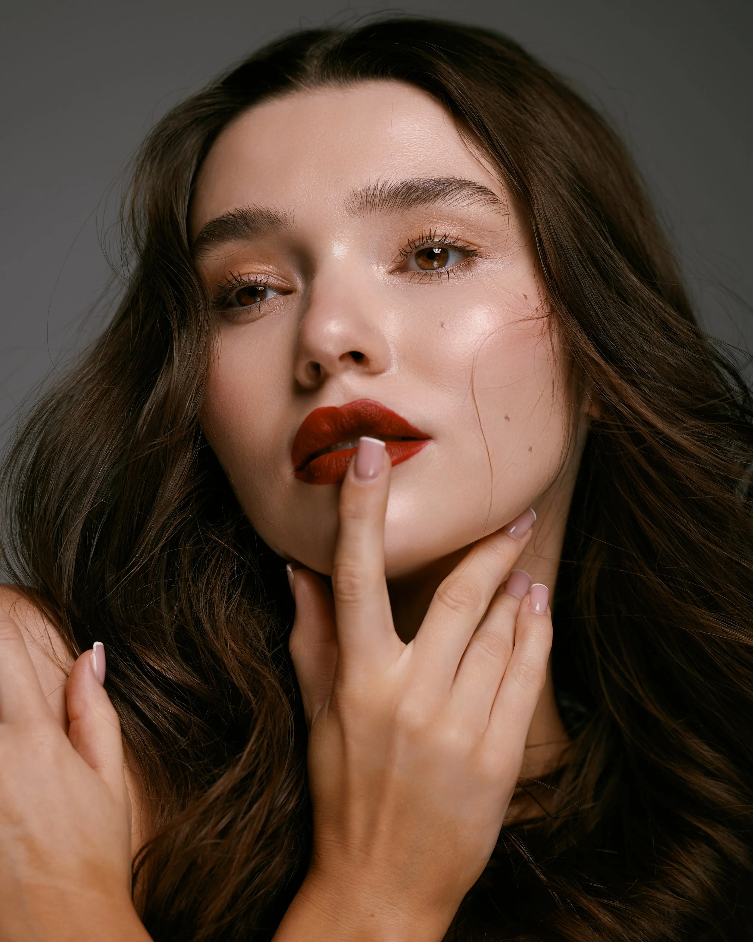 Beauty photography in Los Angeles: red lip, finger to the lips on a dark backdrop, by Moises Martinez
