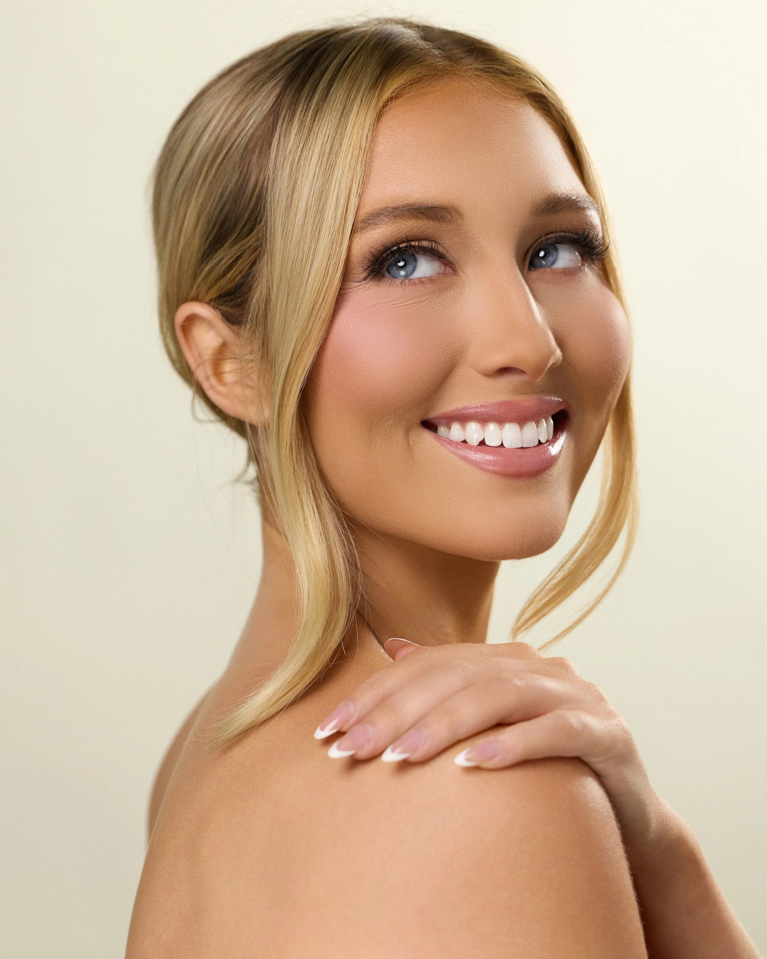 Beauty photography in Los Angeles: bright smile and soft bronzed makeup on a cream backdrop, by Moises Martinez