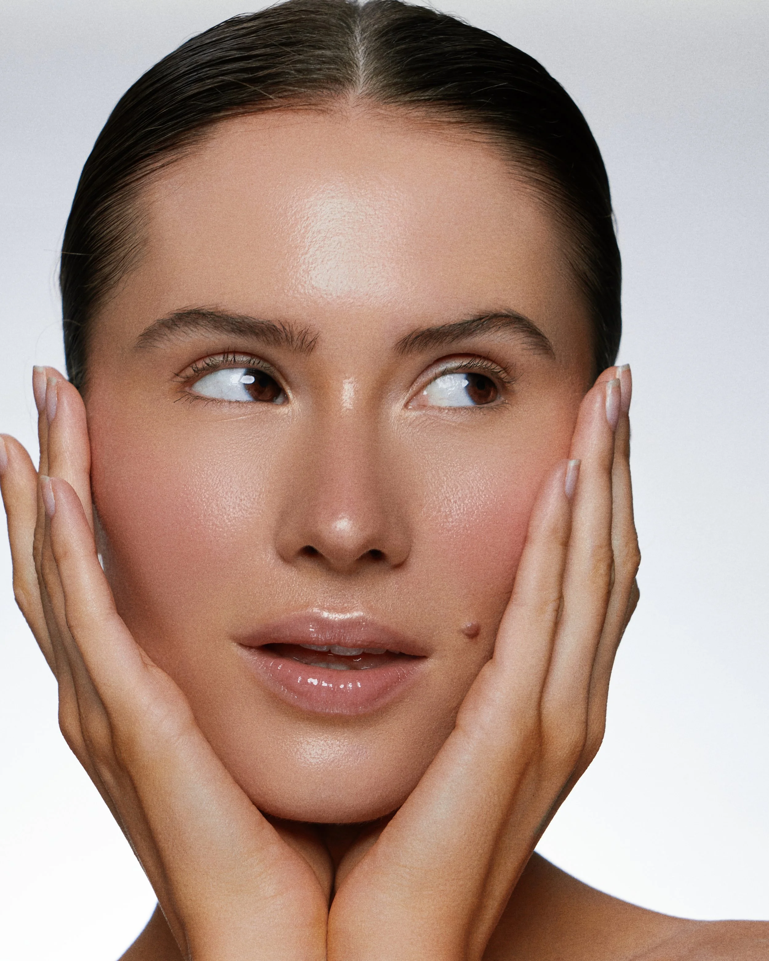 Beauty photography in Los Angeles: slicked-back hair and dewy skin, hands framing the face, by Moises Martinez
