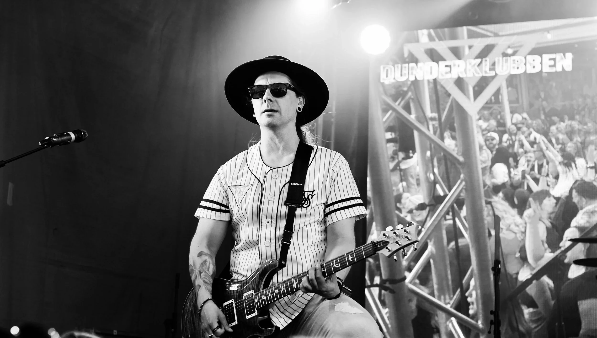 Manlig gitarrist i solglasögon och hatt står på scenen och spelar.