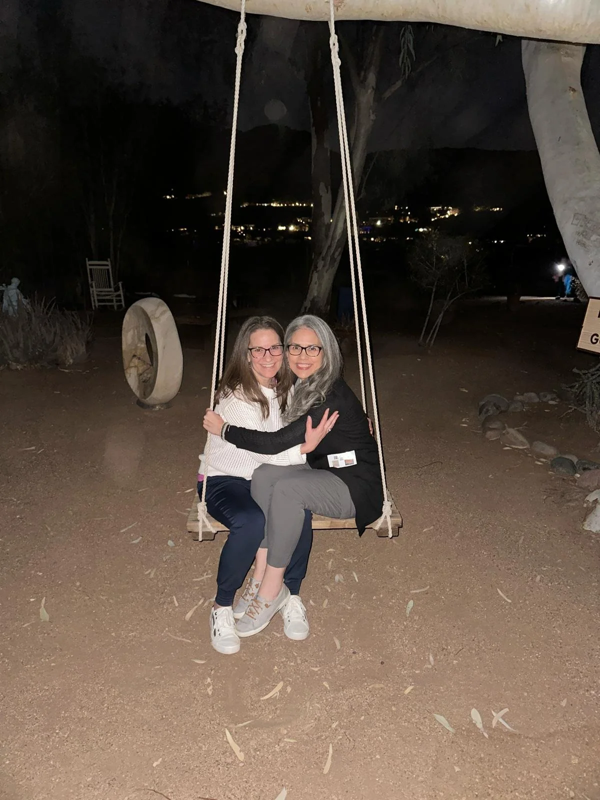 Two people sitting and hugging on a swing at night in an outdoor setting.