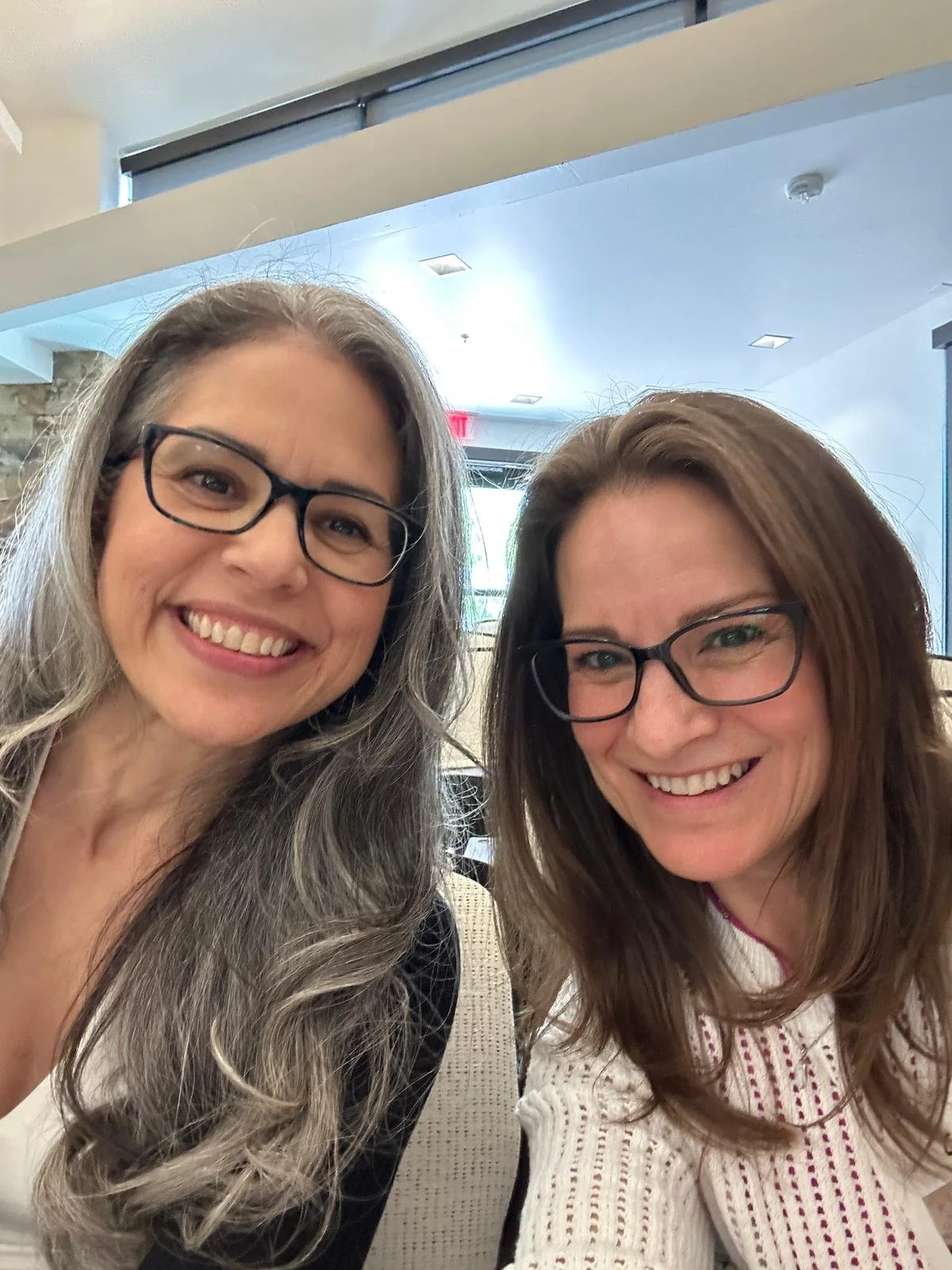 Two women with glasses smiling indoors