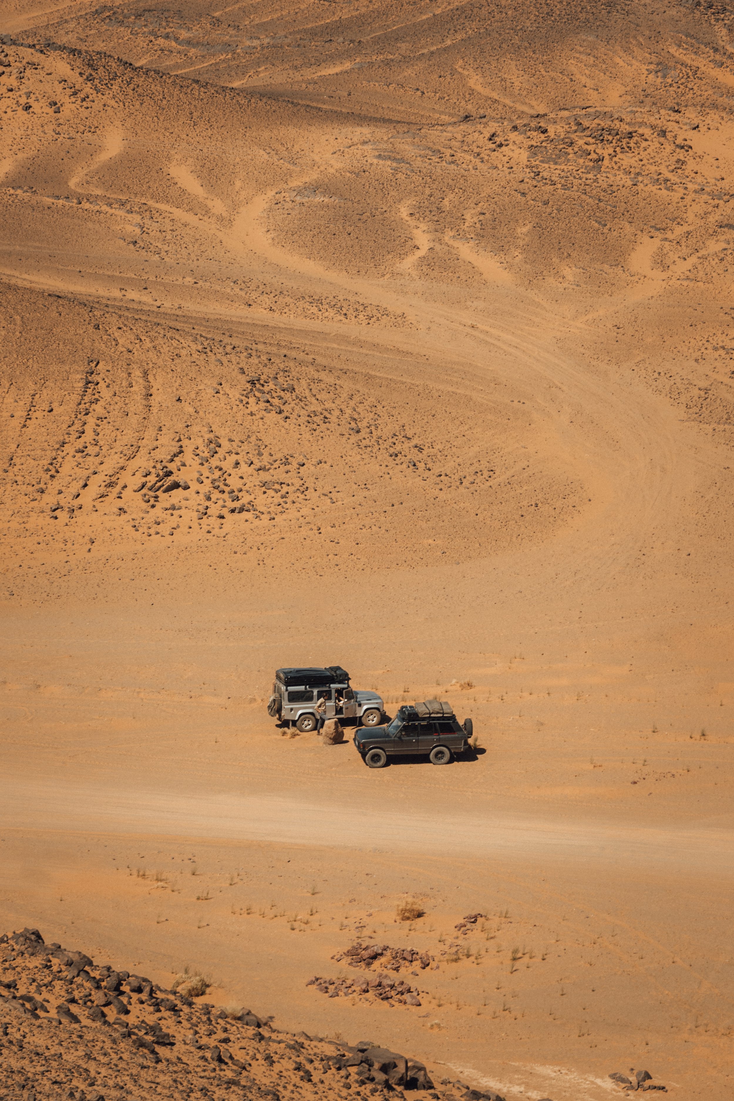 Two off-road vehicles parked on a sandy desert landscape with tire tracks and sparse vegetation.
