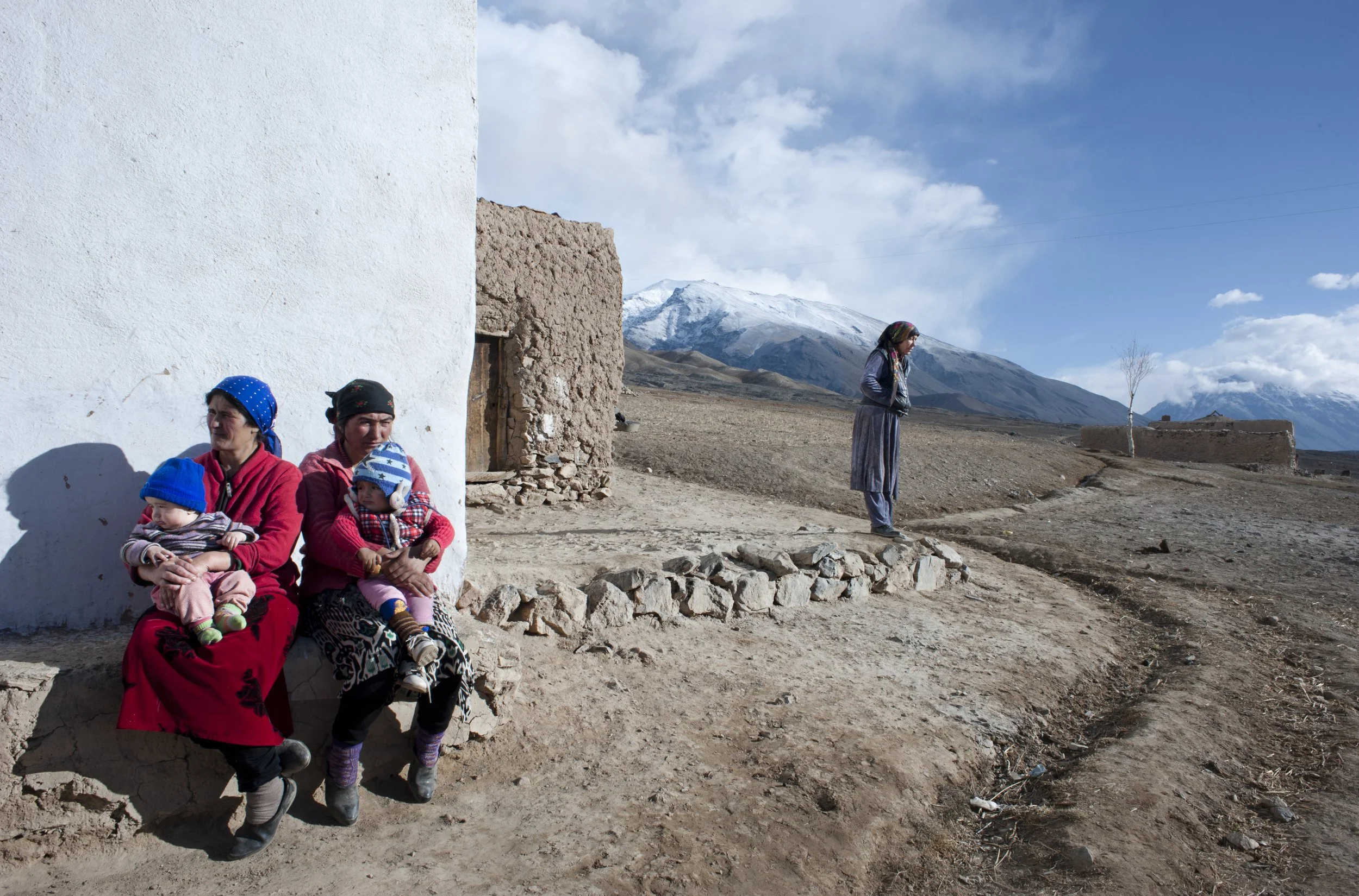 A calm afternoon in the village. Women sit in front of their houses. Here, houses are built with stones and clay mixed with straw. A roof is the most expensive part of a house as people need to import wood from Kirgizstan. During soviet times, it was