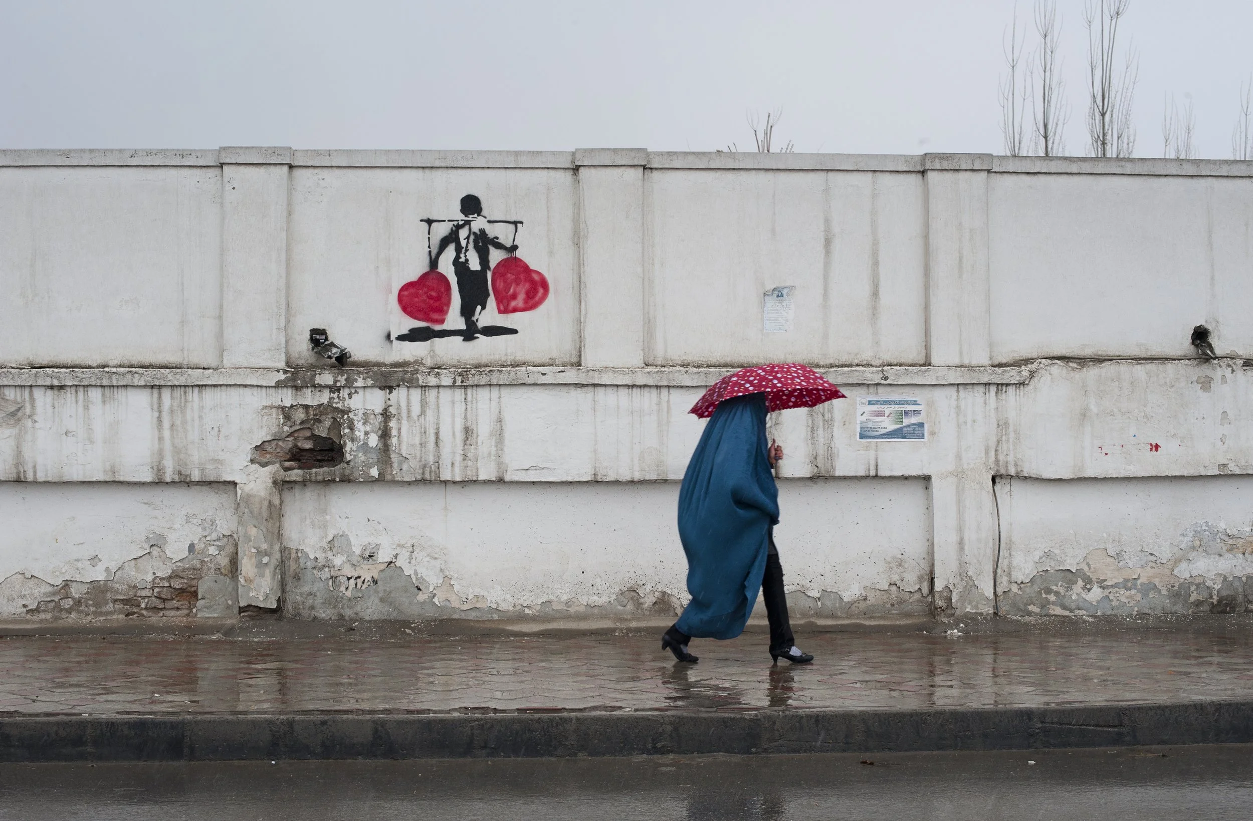 Kabul is a place to be. A woman walking in one of the main street of Kabul. On the wall, Banksys anti-war project. Kabul is a place to be. Anything is possible because everything has to be rebuilt. The city attracts high level war specialists as well
