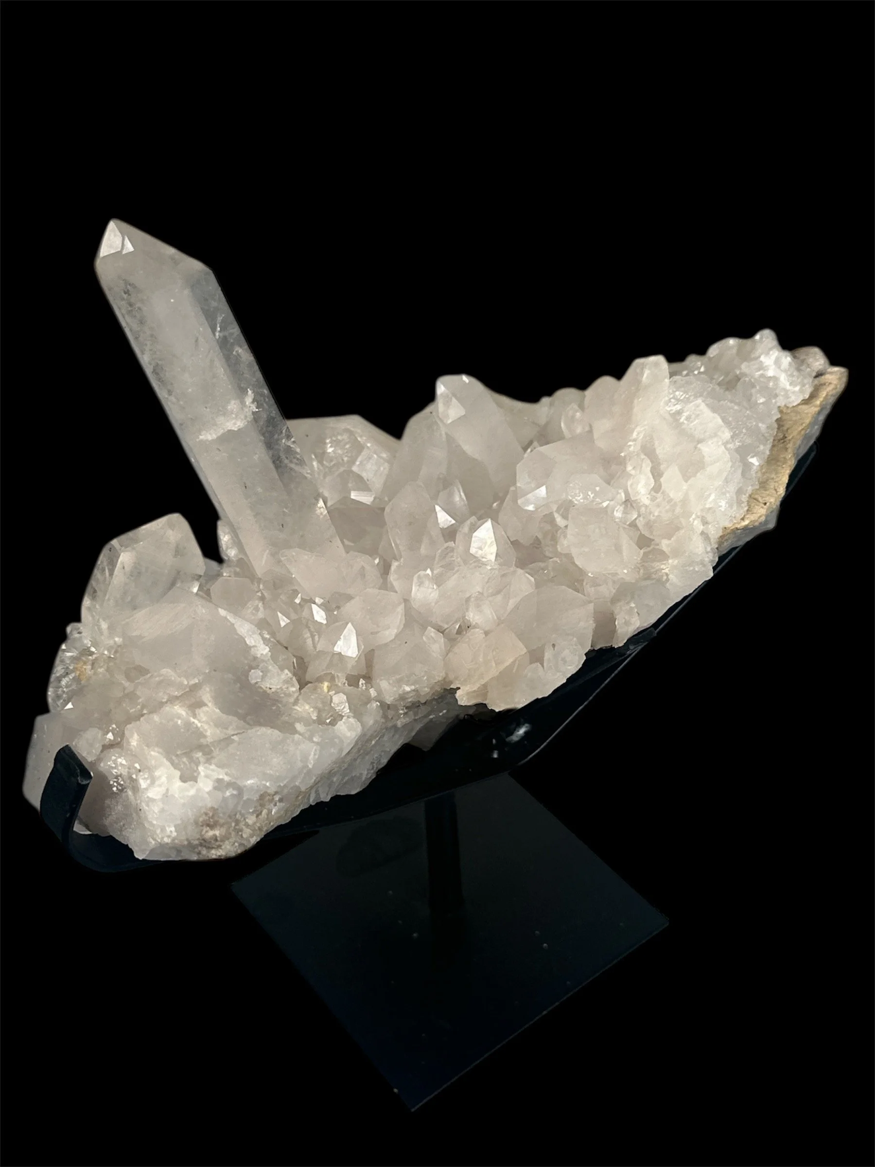 A cluster of clear quartz crystals with one prominent pointed crystal on a black background.