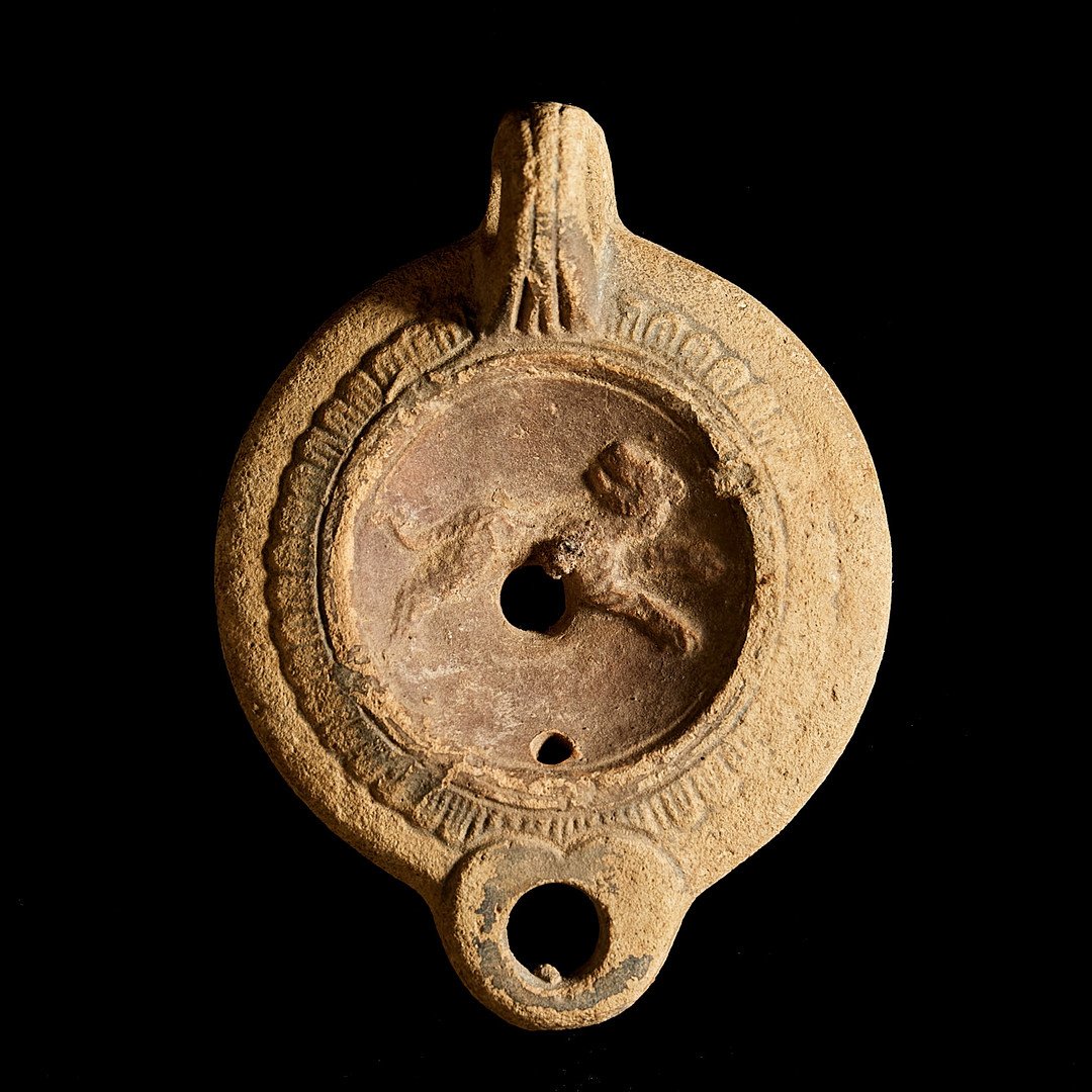Ancient circular terracotta oil lamp with carved inscriptions and a dragon or serpent raised relief, featuring three holes.