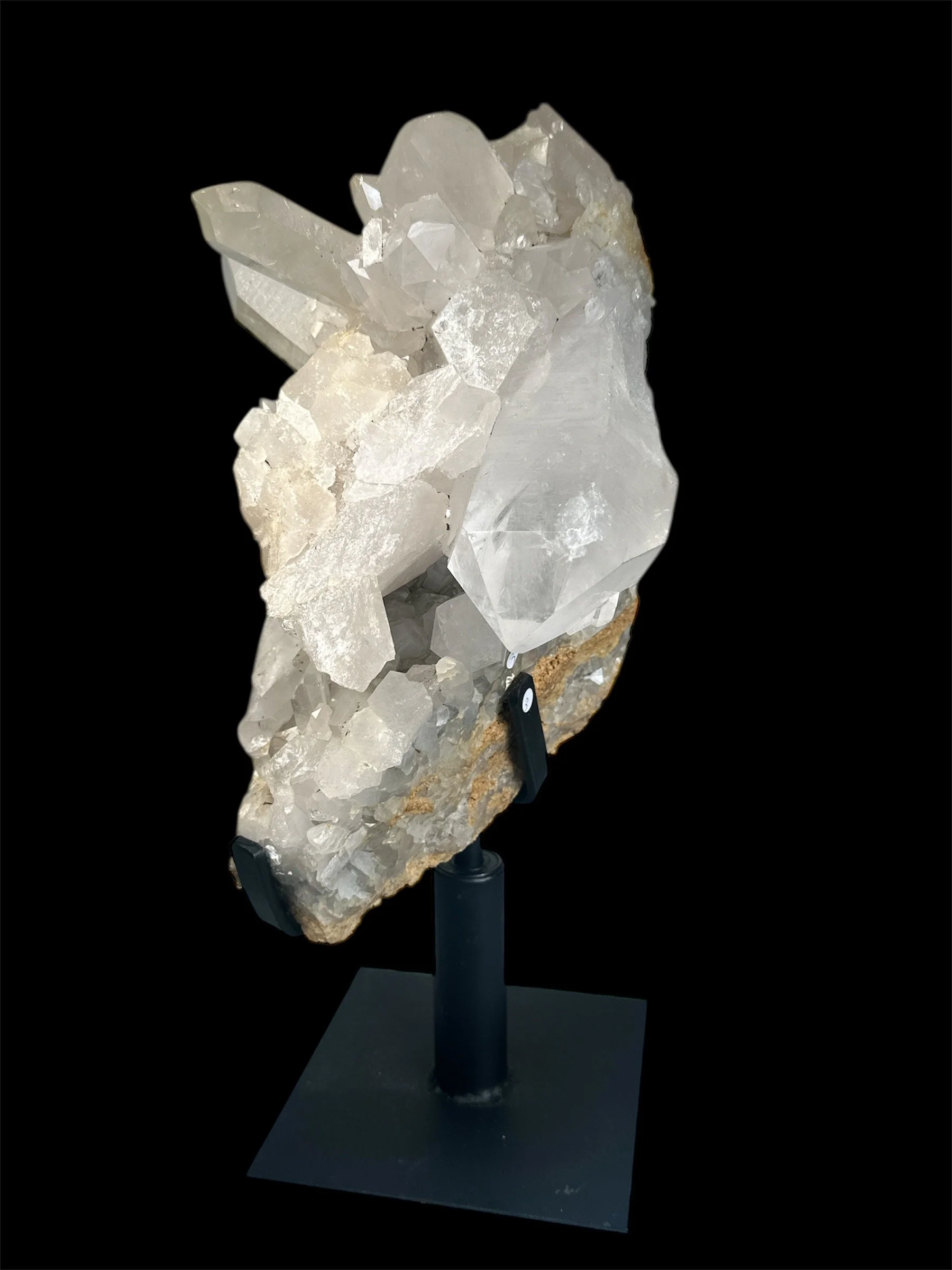 A large, clear quartz crystal with smaller white crystals attached, mounted on a black stand against a black background.