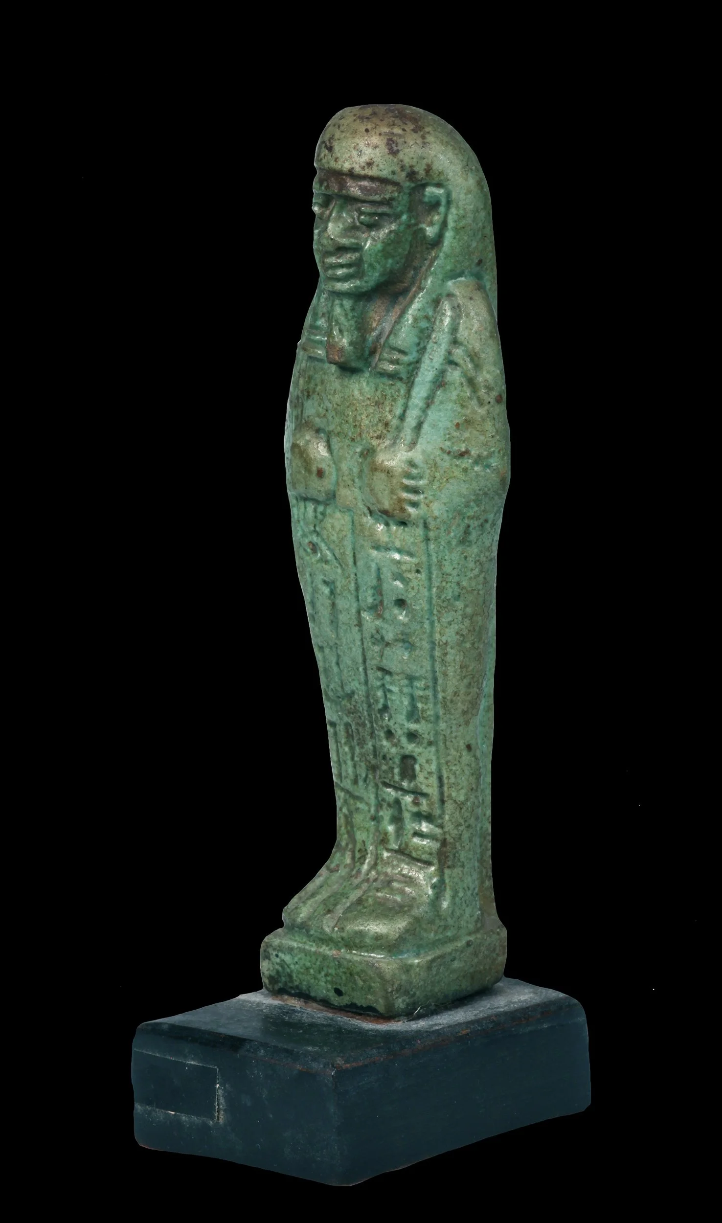 Ancient Egyptian bronze statue of a standing figure with a headdress, holding a staff, facing left, on a black base.