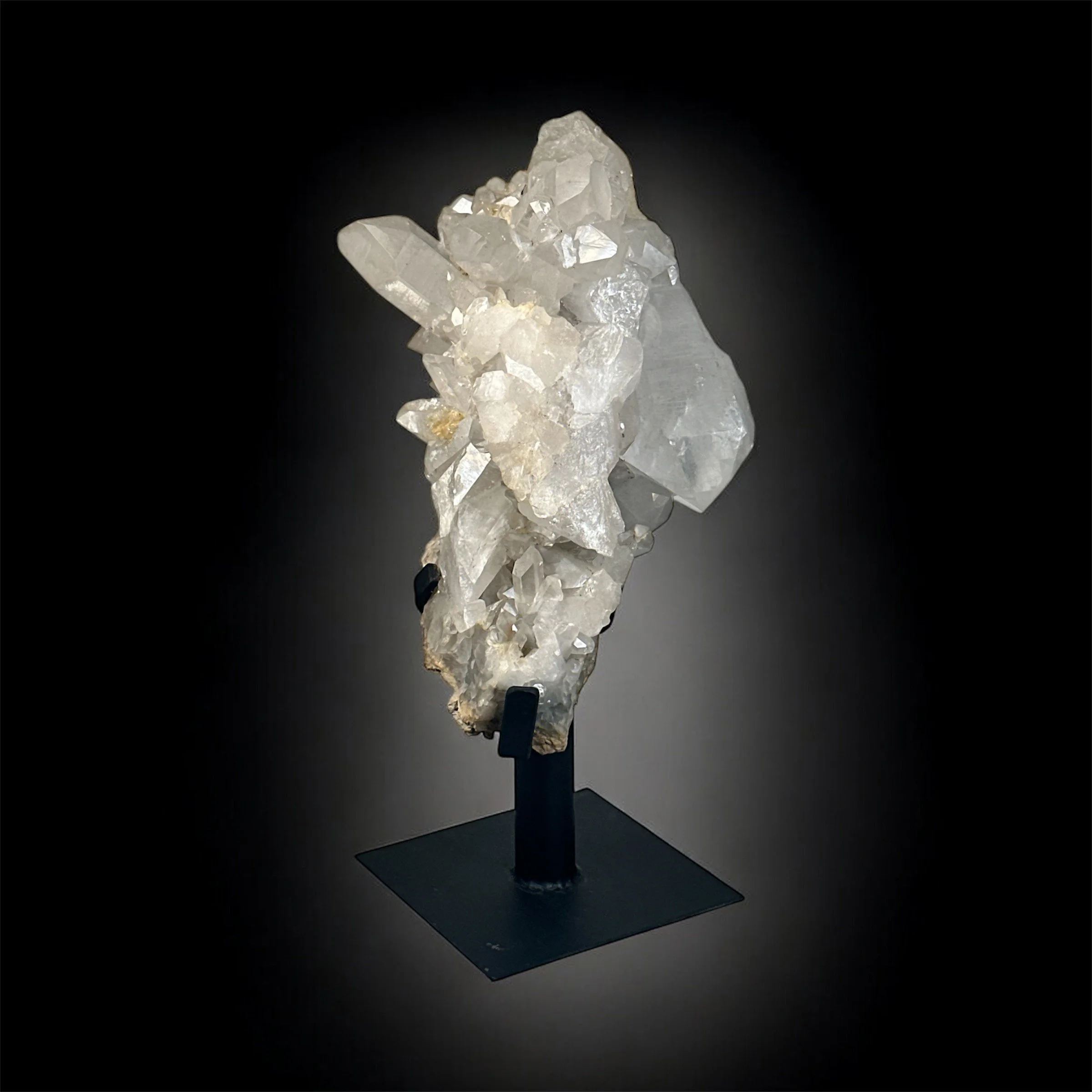 A cluster of white and transparent quartz crystals displayed on a black stand against a dark background.