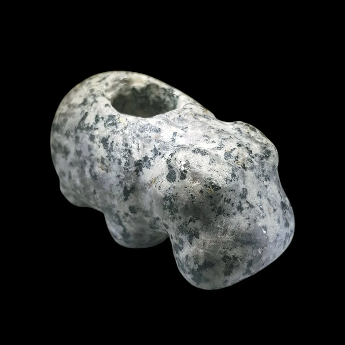 A small, irregularly shaped stone carved into a hippopotamus, viewed against a black background.