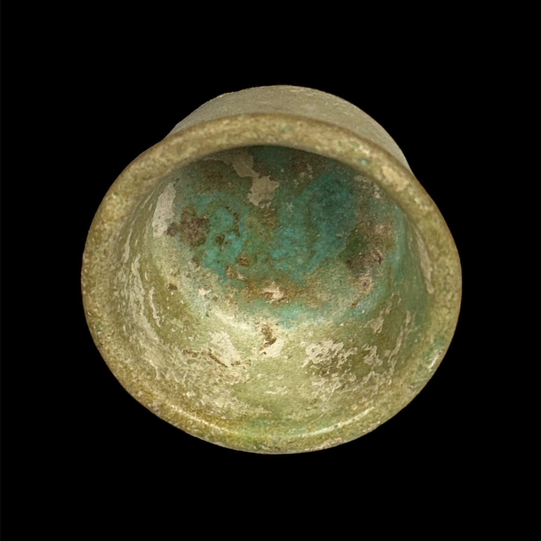 Close-up of an ancient, weathered metal coin with green patina, viewed from above against a black background.