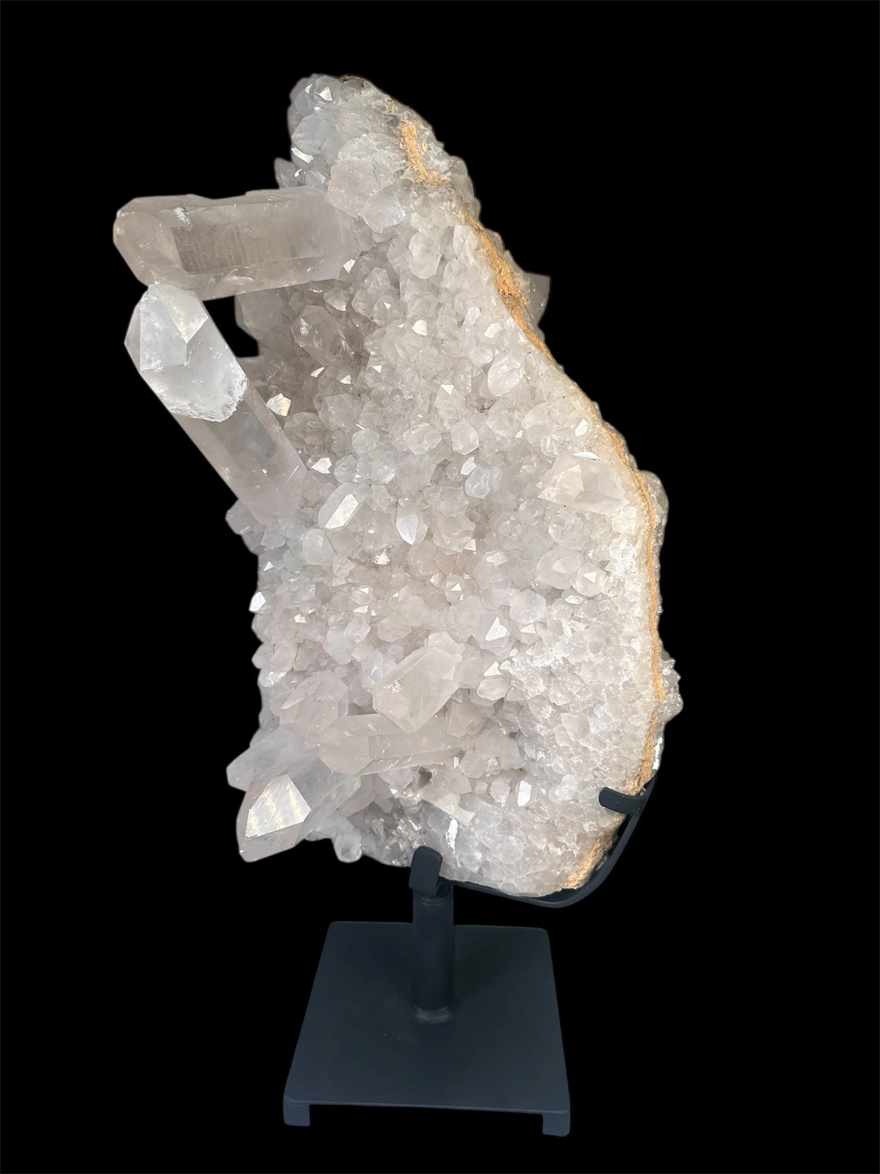 A white crystalline mineral specimen on a black stand, featuring large and small crystal formations with a rough edge and a gold-colored vein running through some of the crystals.