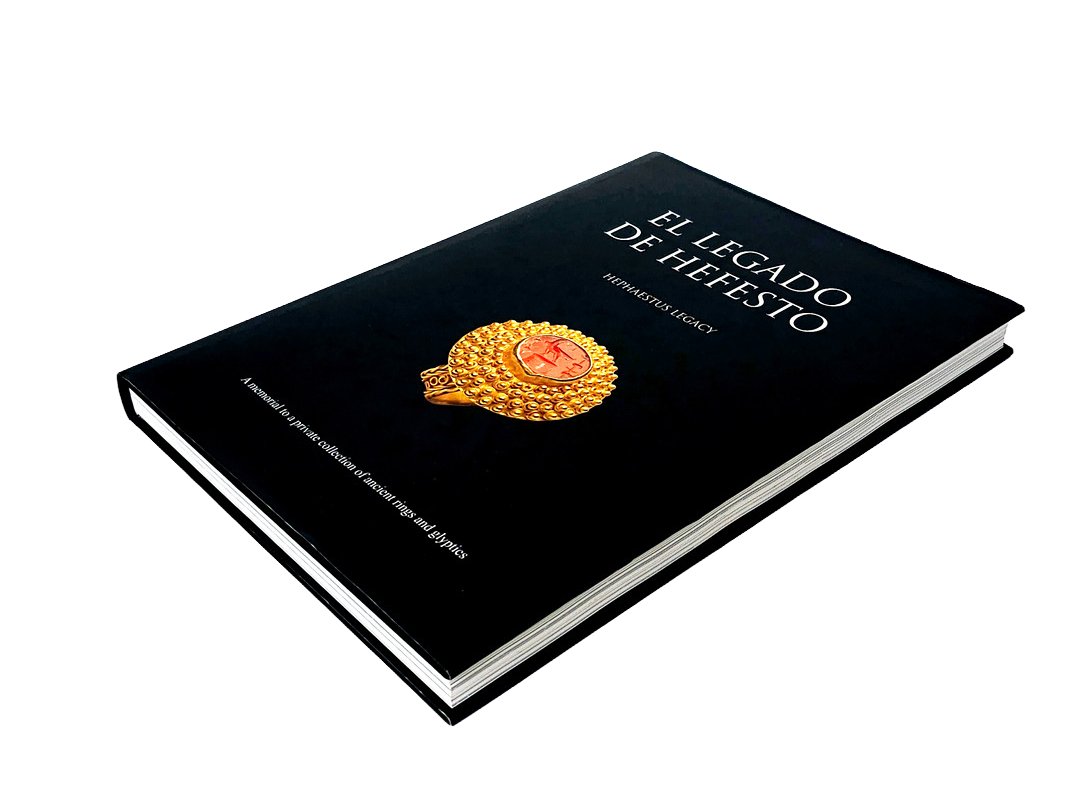 A black book titled 'El Legado de Hefesto' with a gold and red circular medal or badge on the cover.