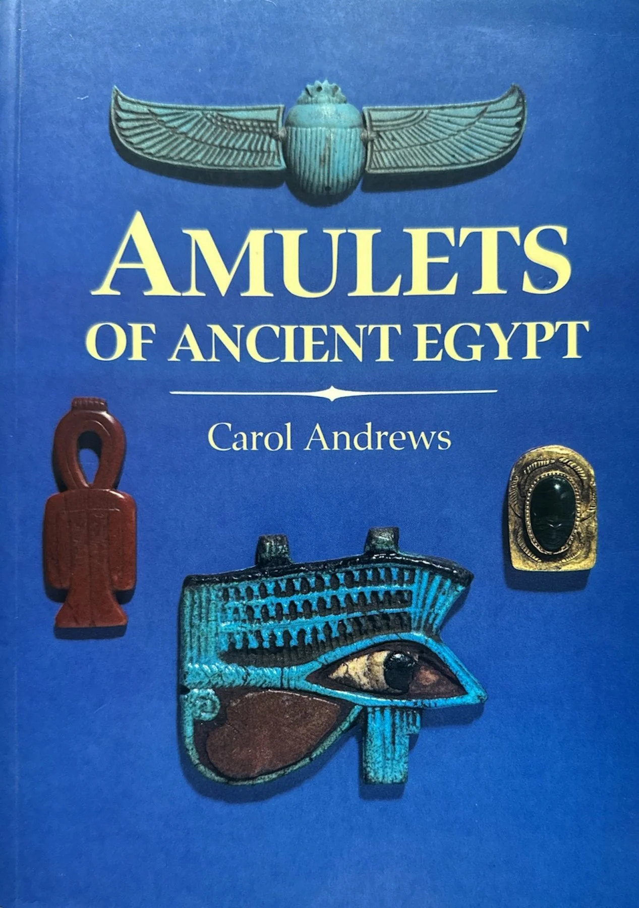 Cover of the book titled 'Amulets of Ancient Egypt' by Carol Andrews, featuring images of Egyptian amulets including a scarab beetle, an eye, and other artifacts, set against a blue background.