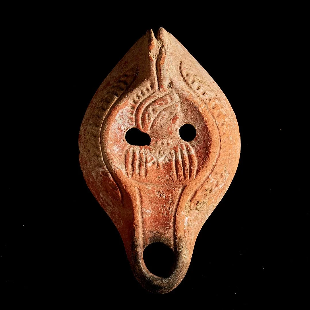 Ancient terracotta figurine with carved face and two holes for eyes, part of tribal or archaeological artifacts.