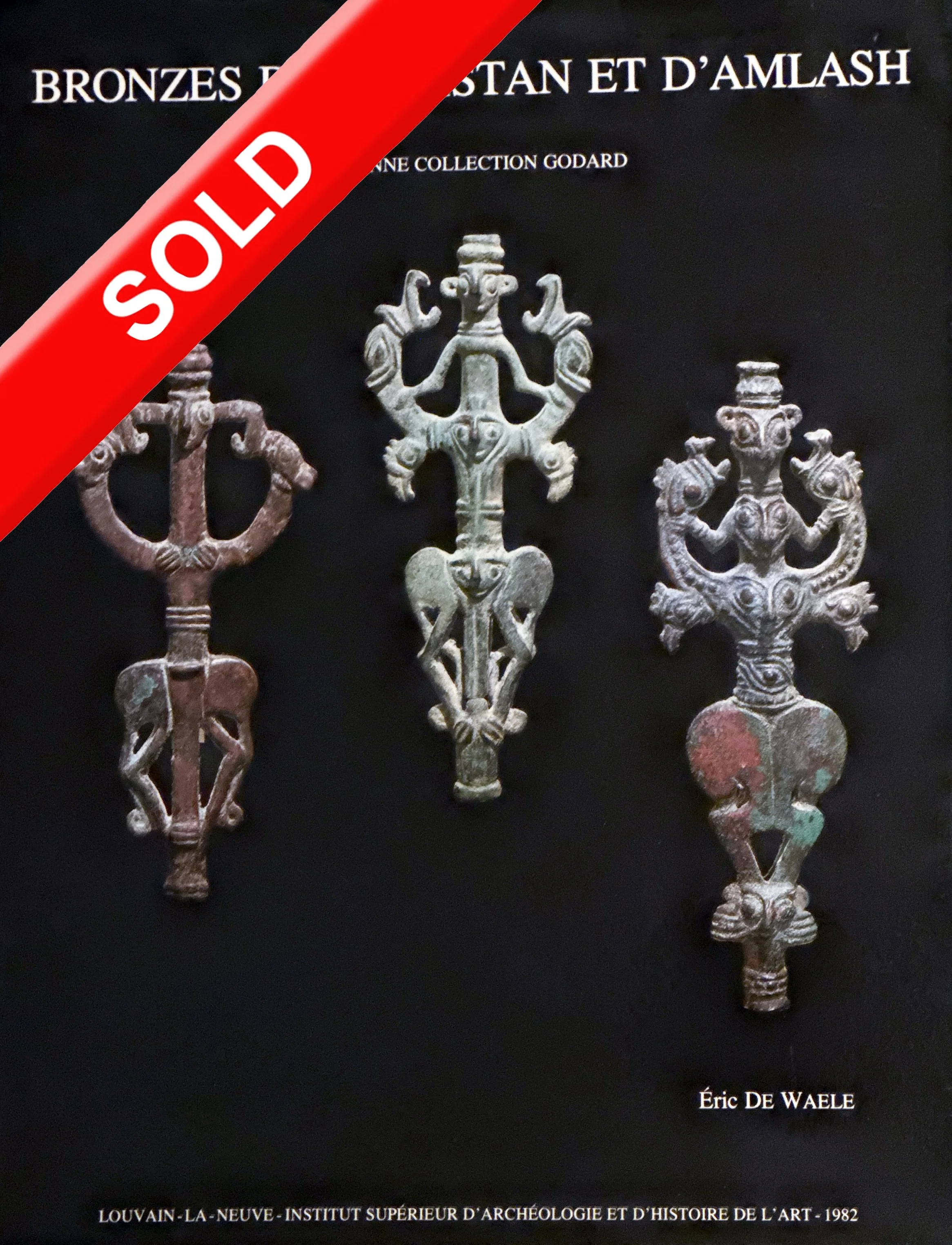 Photograph of three ancient Luristan metal amulets on a black background with French text. The amulets are bronze, decorated with intricate patterns, and arranged vertically center. A red 'SOLD' banner overlays the top left corner.