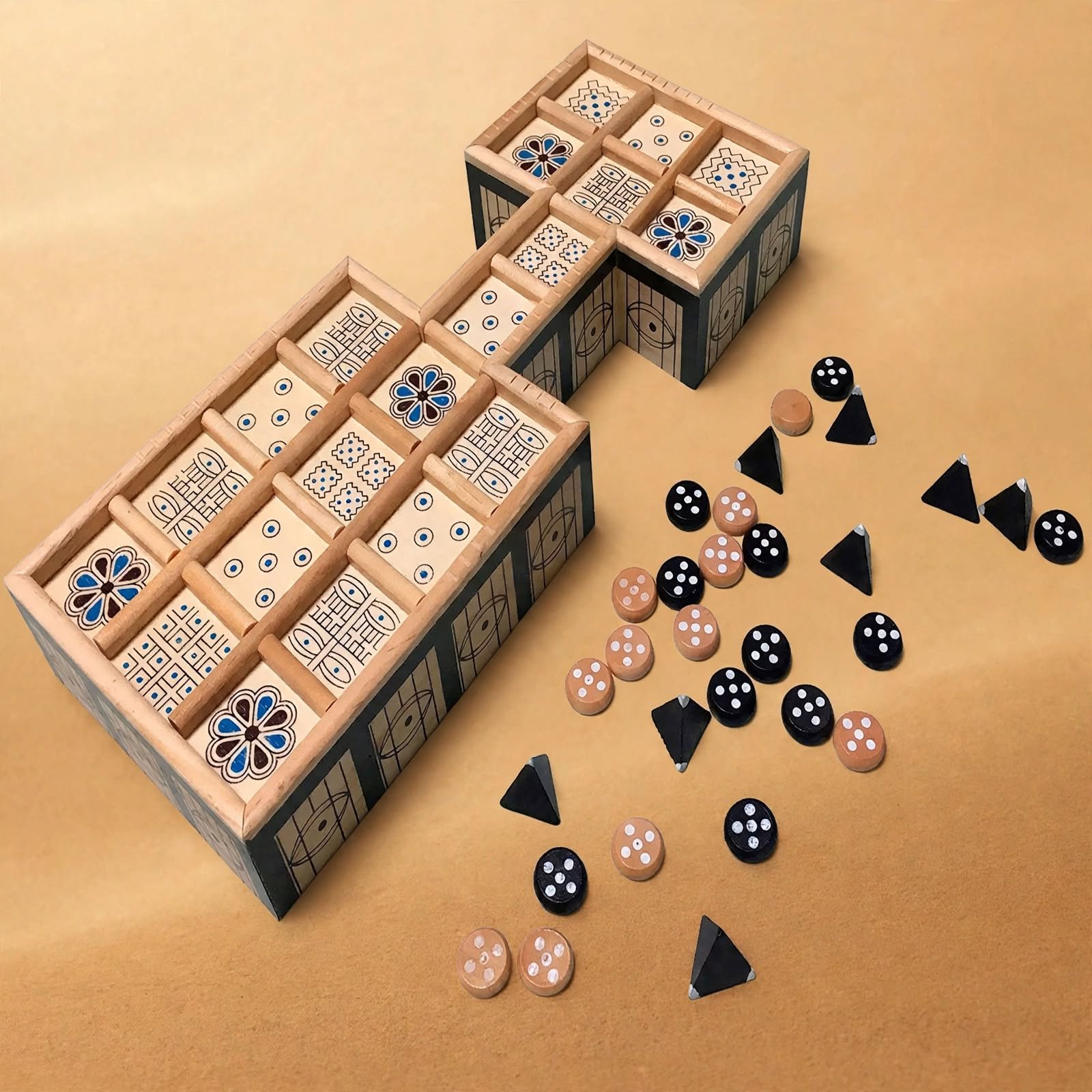 Board game with black and beige dice, and a container with compartments holding decorated tiles, set on a tan surface.