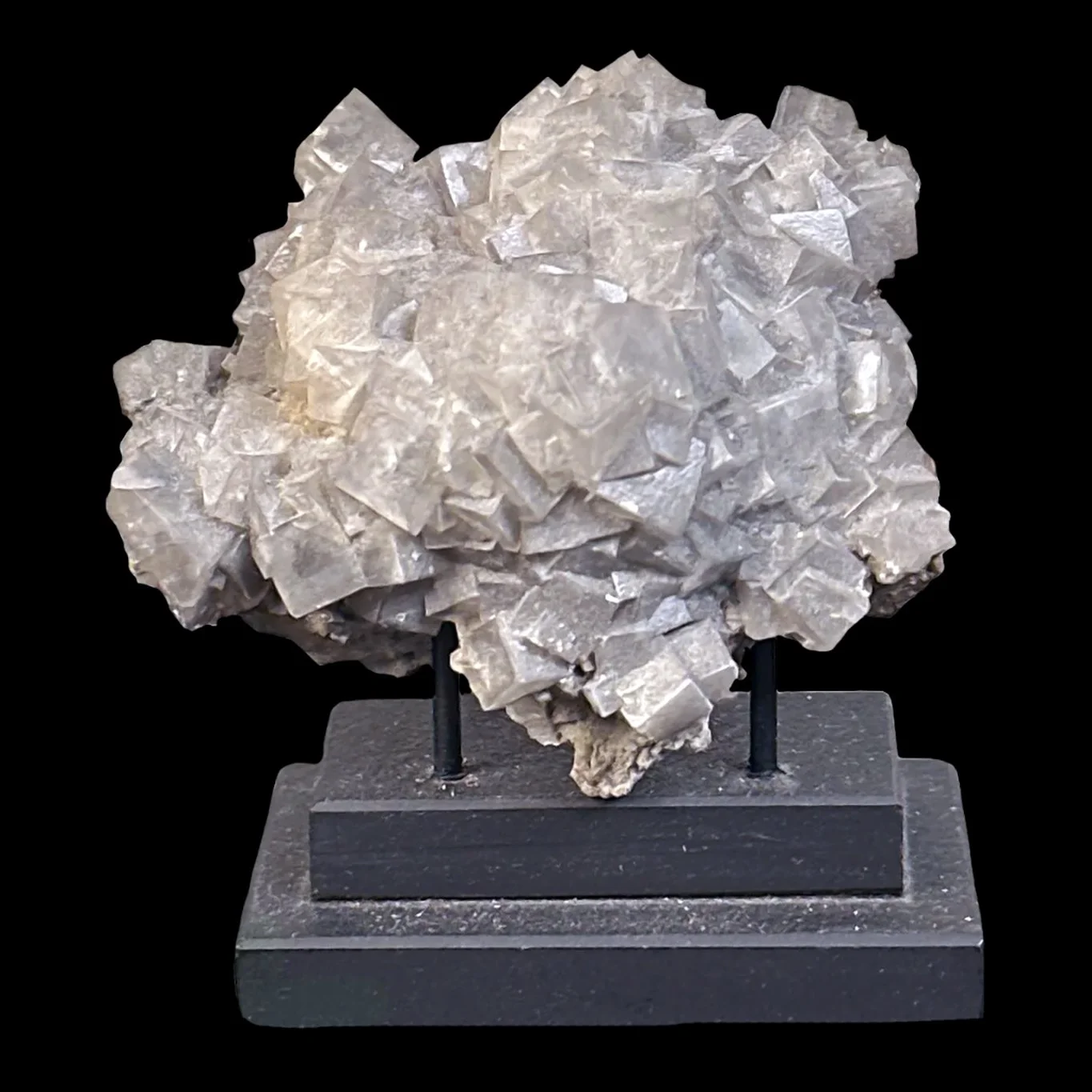 A crystalline mineral specimen with a rough, layered texture displayed on a black stand against a black background.
