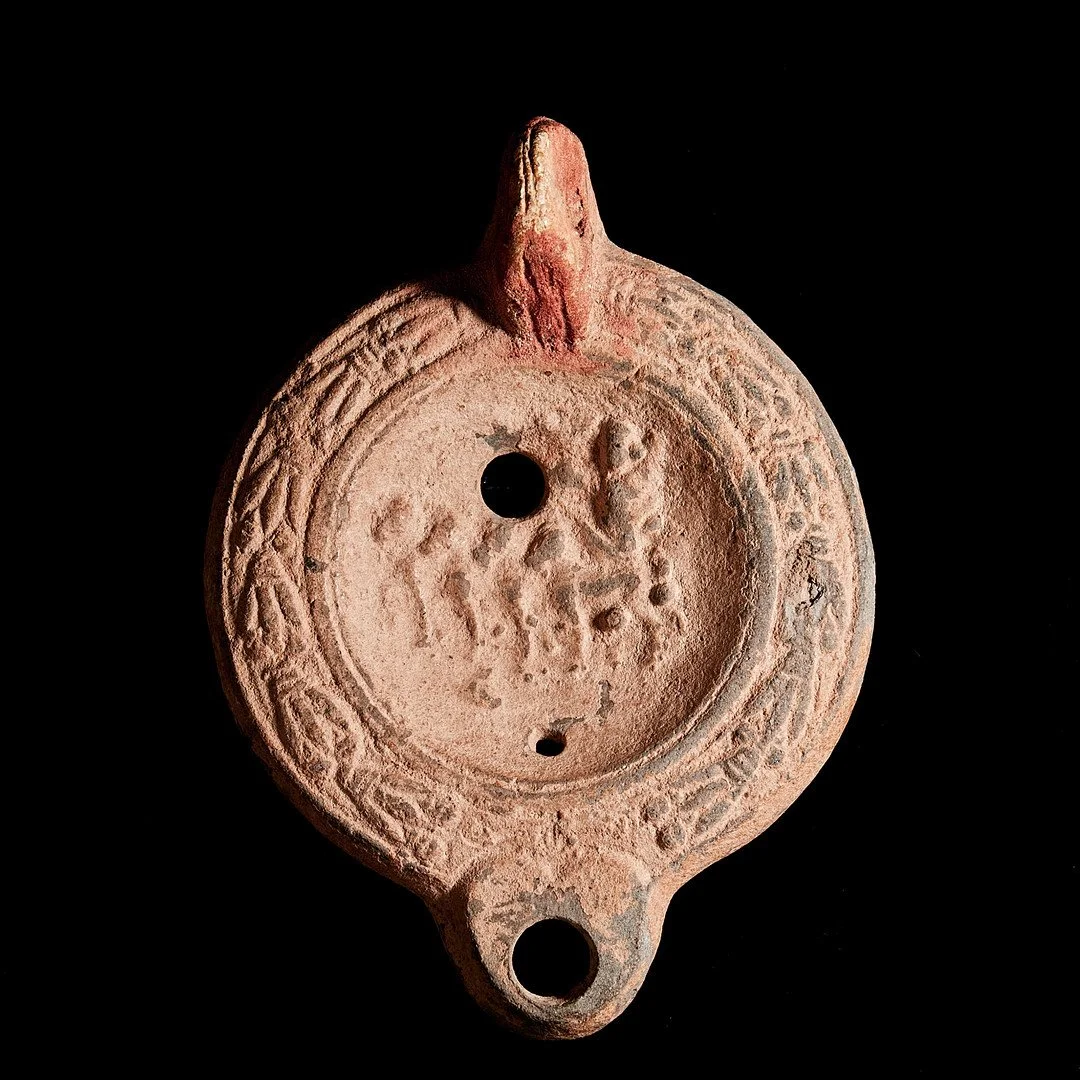 Ancient clay or ceramic artifact with circular design and inscriptions, featuring three holes, against a black background.