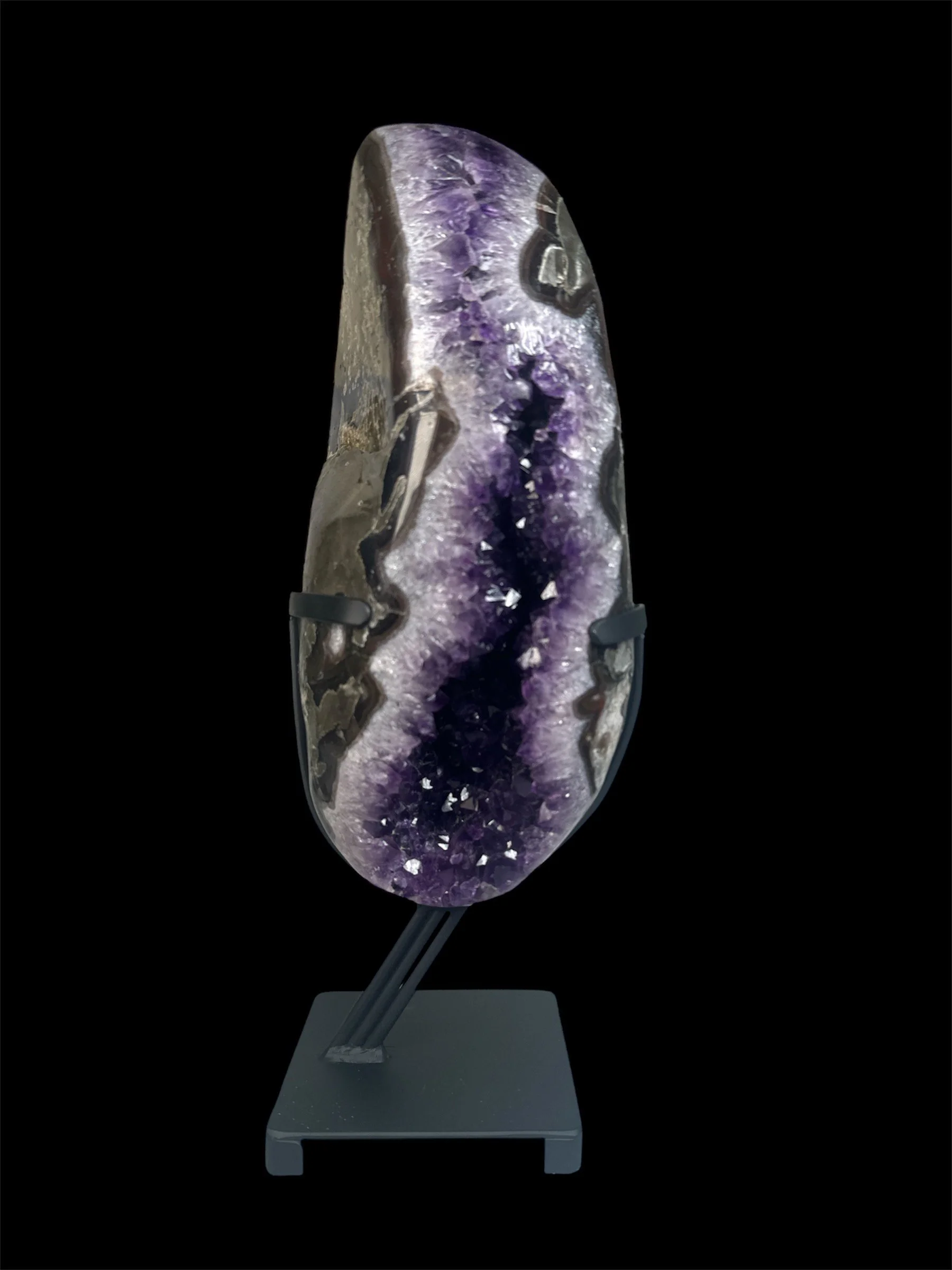 A large polished amethyst geode on a black stand against a black background.
