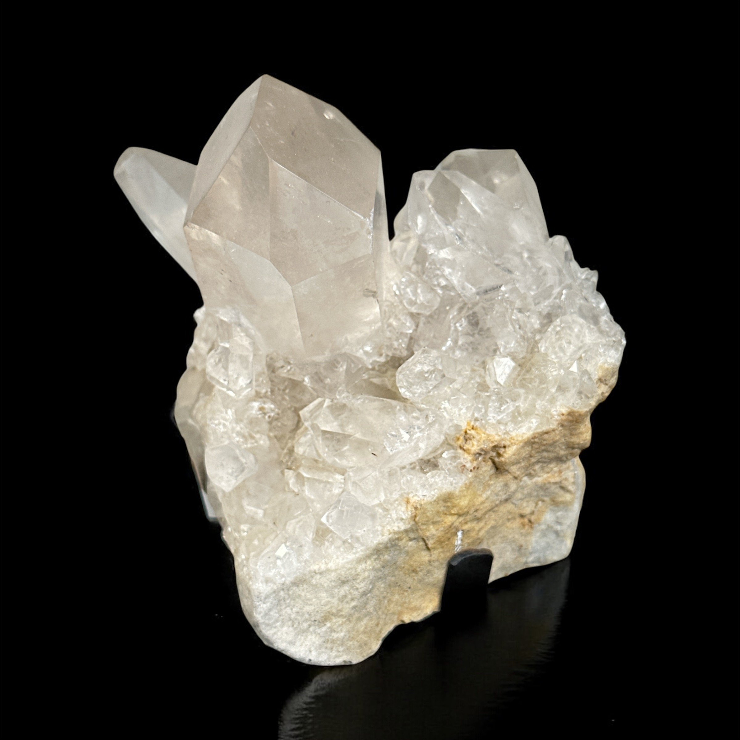 A cluster of clear, well-formed quartz crystals growing on a rough, beige matrix