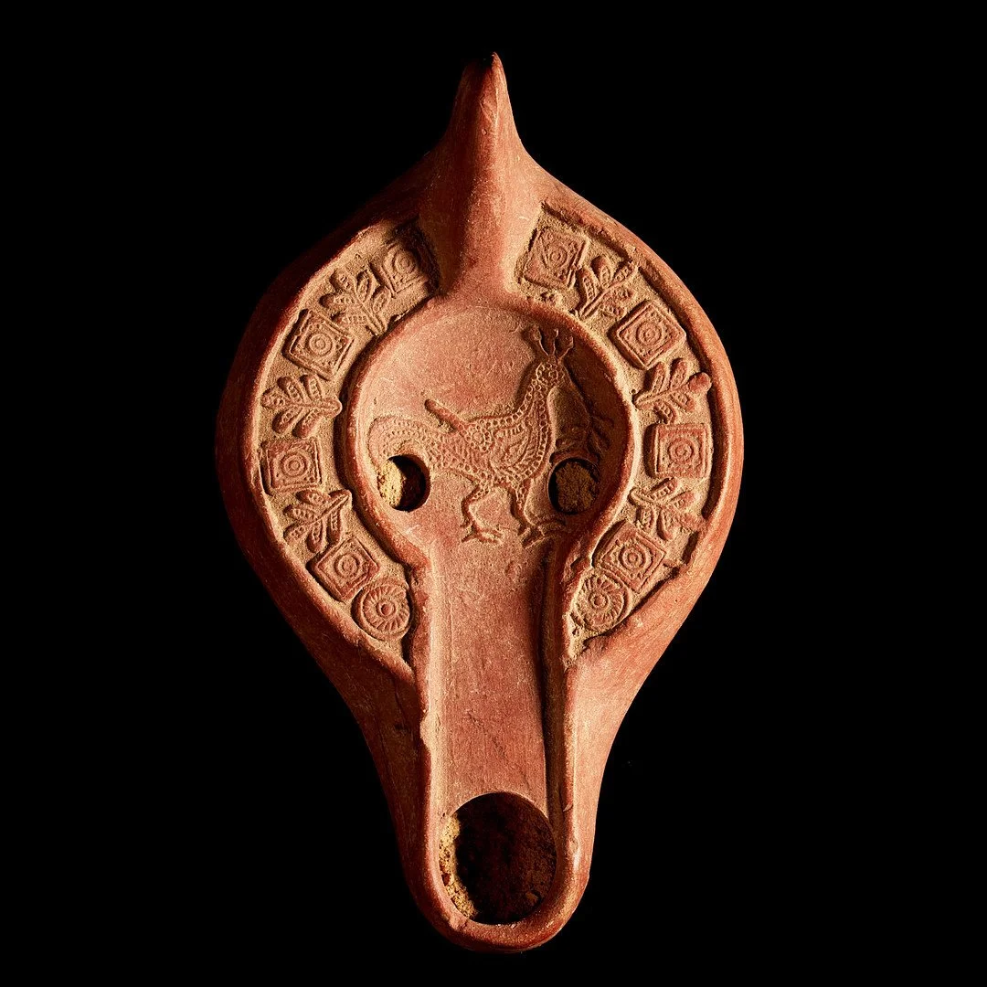 Ancient terracotta artifact with carved geometric patterns and a central figure of an animal, possibly a horse or deer, on a black background.
