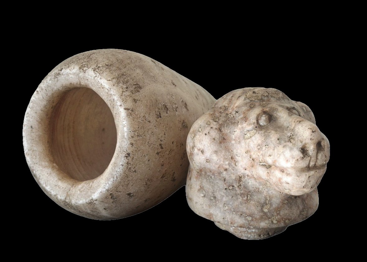 Ancient carved stone artifact, possibly a seal or sculpture, with a hollow cylindrical piece and a carved animal head resembling a lion or feline.