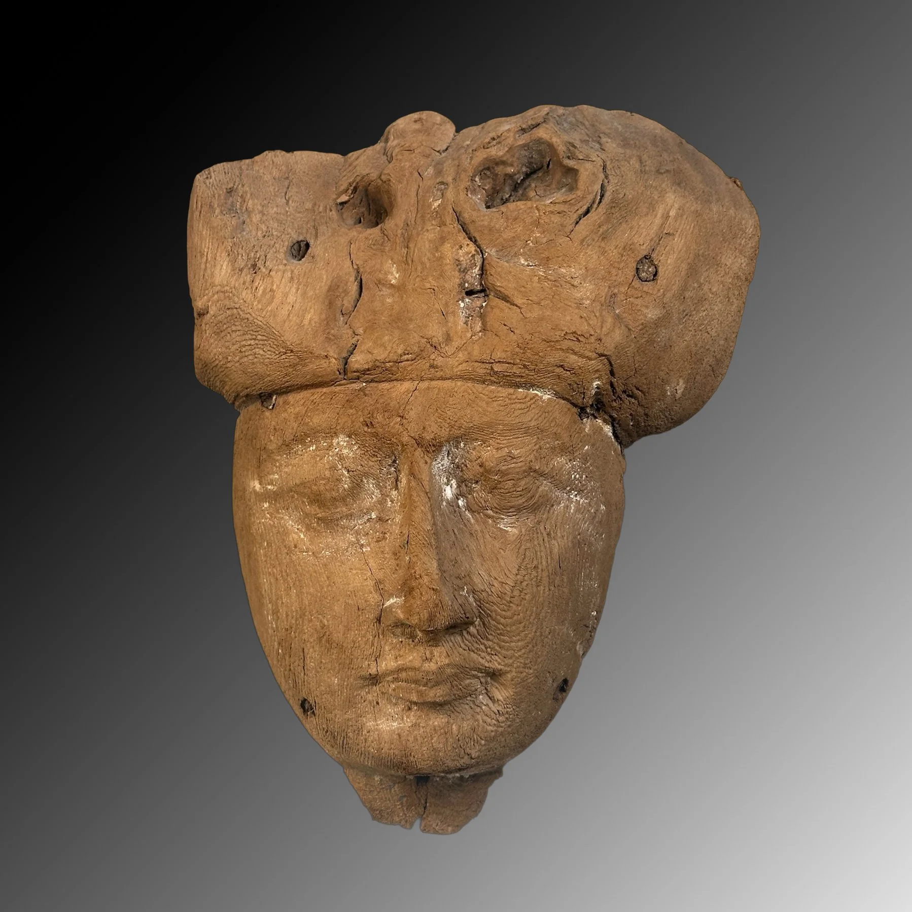 Ancient wooden artifact with a carved face resembling a human, against a dark gradient background.