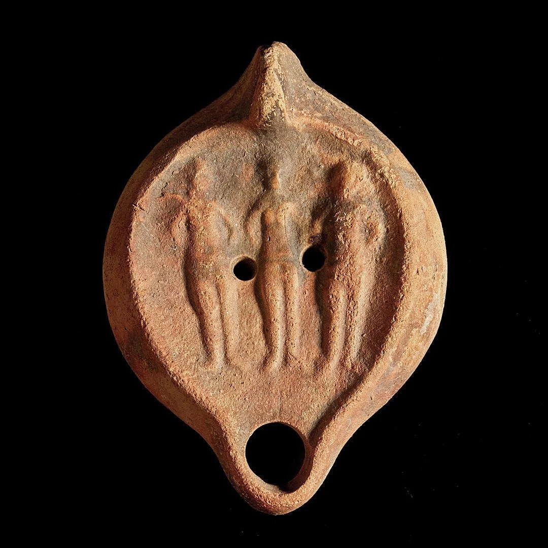 Ancient terracotta oil lamp with three human-like figures and holes, possibly a ritual object or ornament.