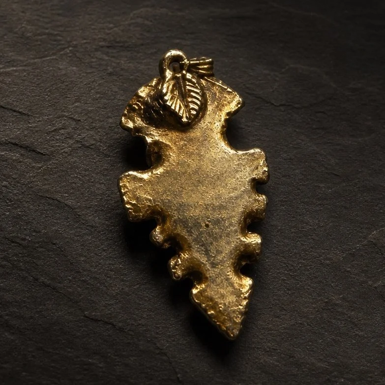 A gold pendant in the shape of the map of the state of Georgia with a small loop at the top for attaching to a chain, placed on a dark textured surface.