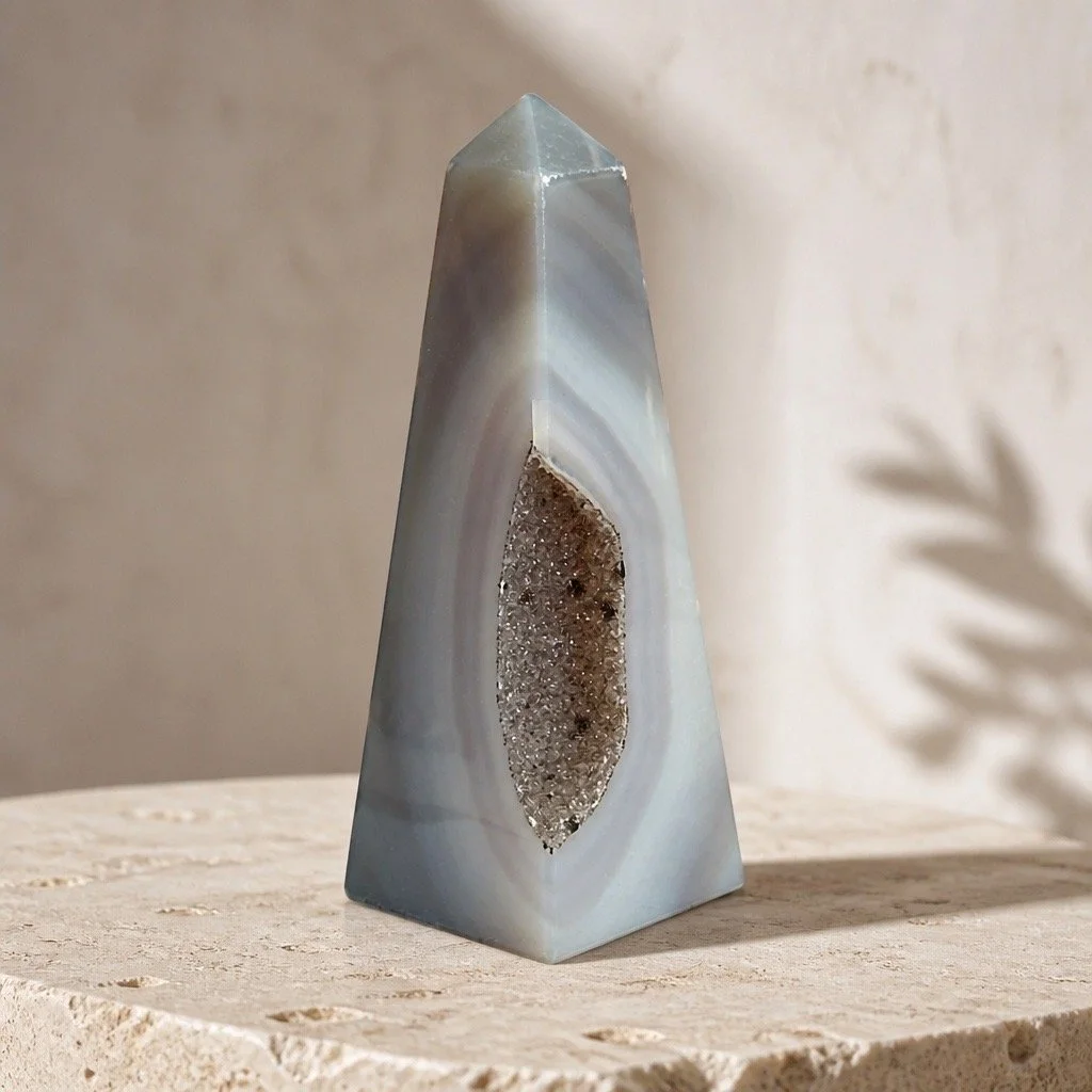 A tall, pyramid-shaped stone sculpture with a textured, geode-like interior, placed on a beige stone surface.