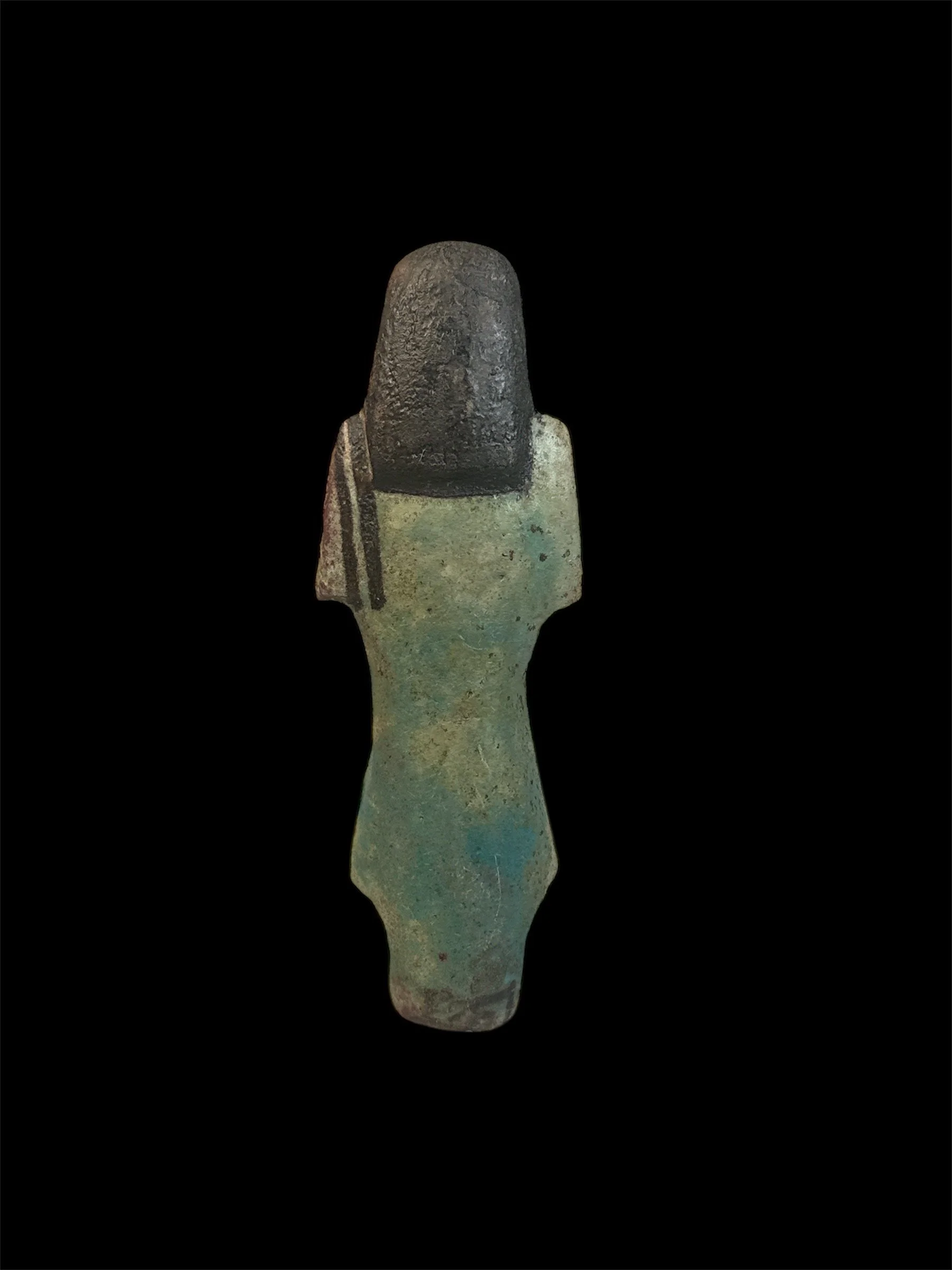 Ancient green and black stone artifact, resembling a figurine or statue, against a black background.