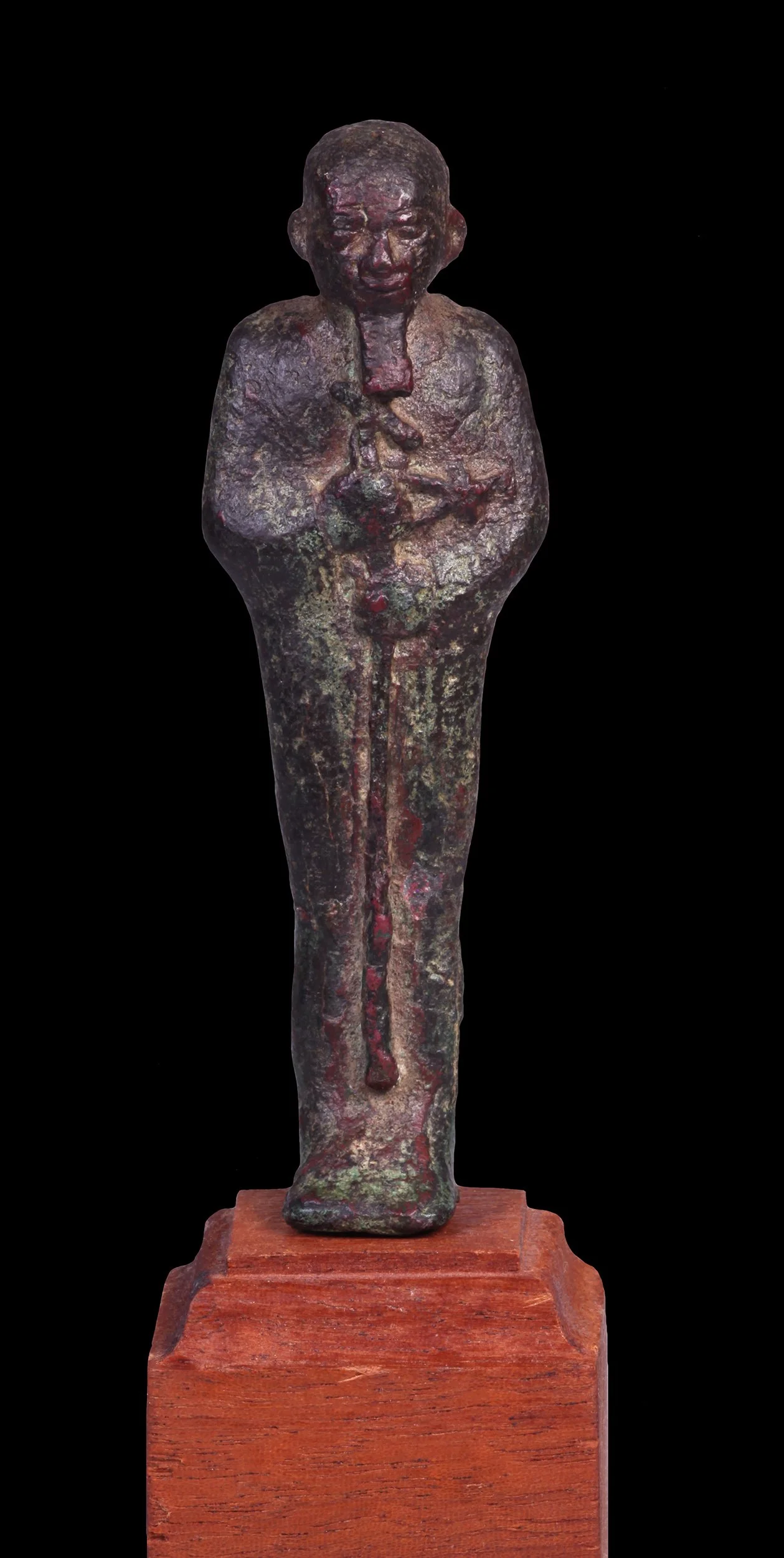 A bronze sculpture of a standing man with a weathered surface, placed on a wooden pedestal against a black background.
