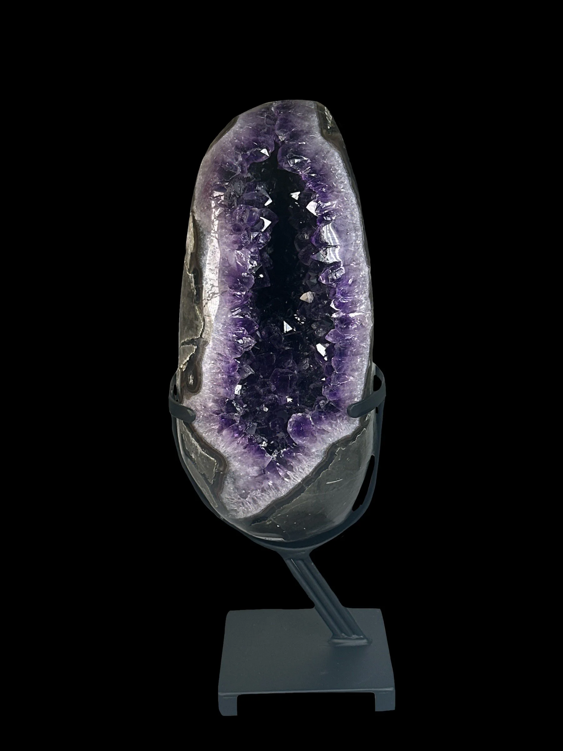 A polished purple amethyst geode displayed on a black stand against a black background.