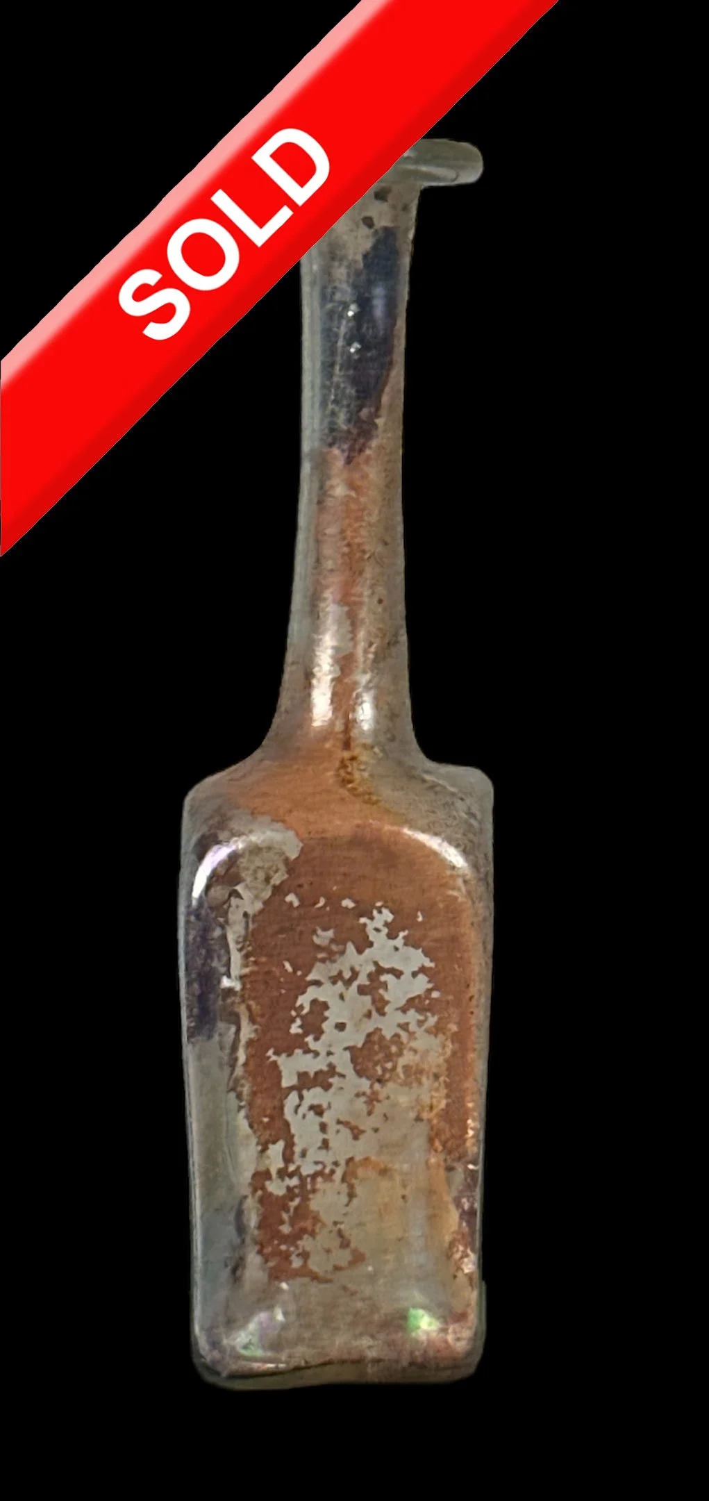 A vintage glass bottle with a long neck and a rectangular body, showing signs of rust and corrosion, against a black background. The bottle has a red