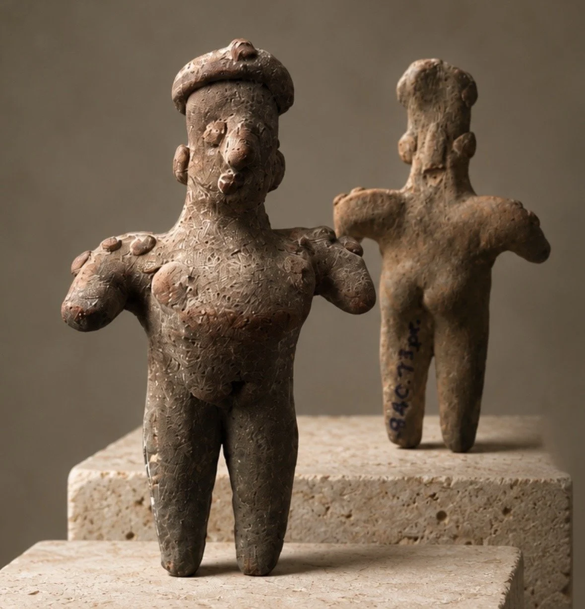 Two ancient terracotta figurines of human figures with exaggerated features, Jalisco, Colima, standing on stone pedestals.