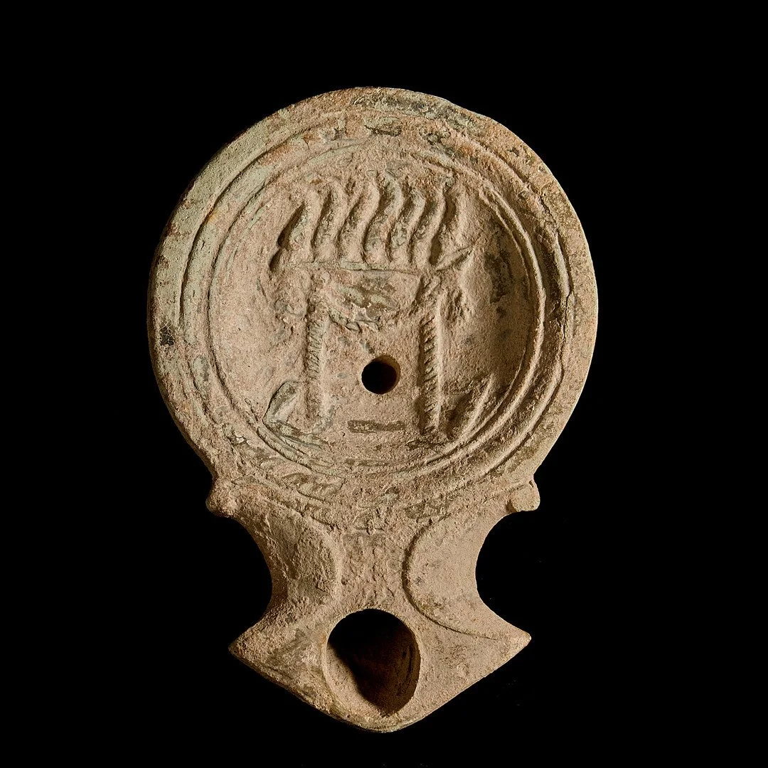 Ancientterracotta oil lamp with circular design, central hole, and carved patterns, against a black background.
