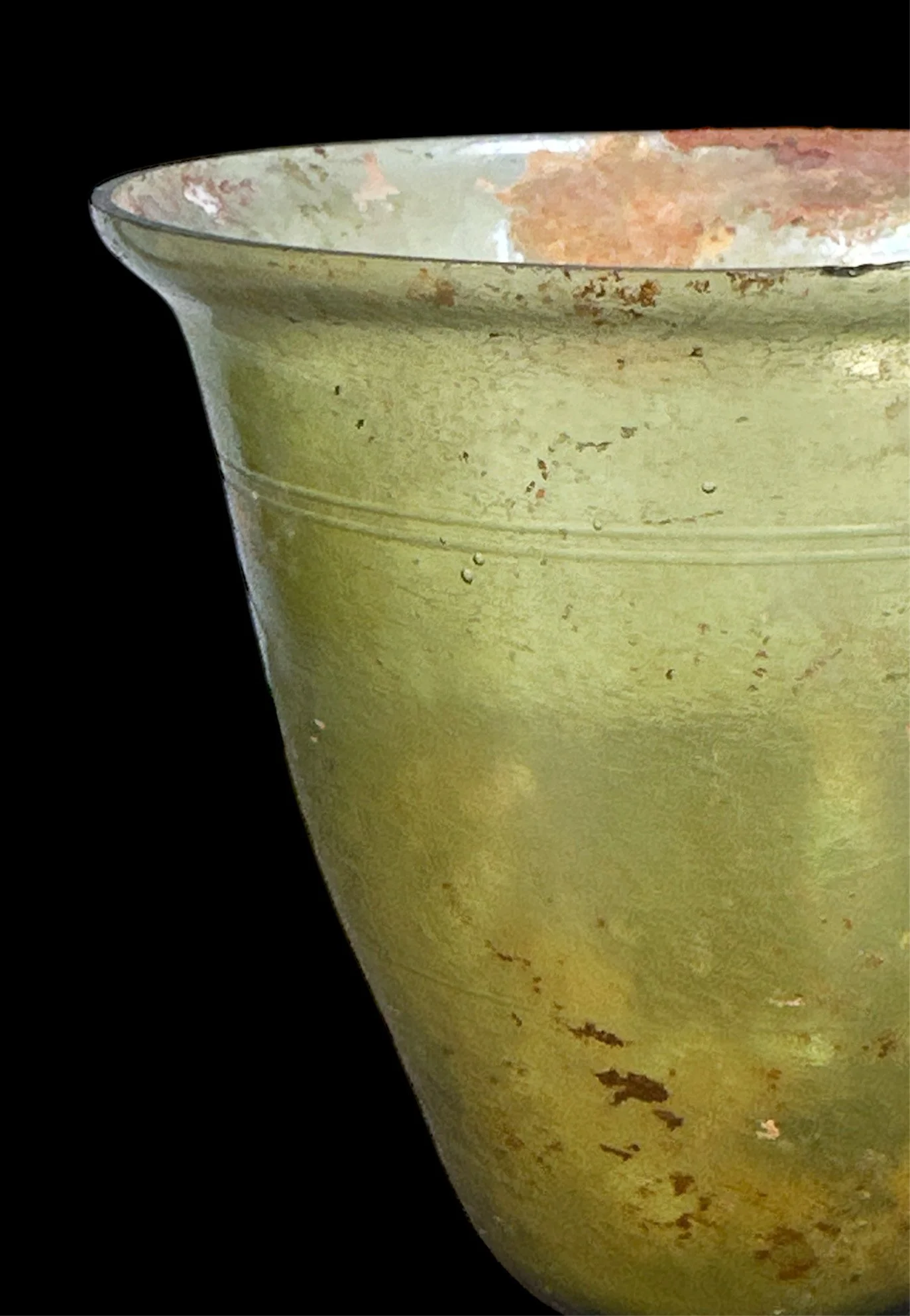 Close-up of a weathered, olive-green ceramic or metal pot with a wide rim against a black background.
