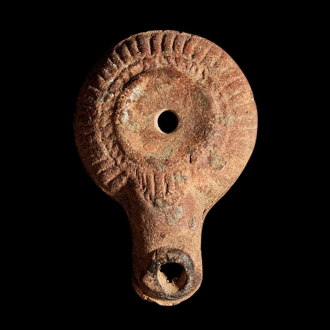 Ancient clay spindle whorl with a central hole and textured surface, isolated on black background.