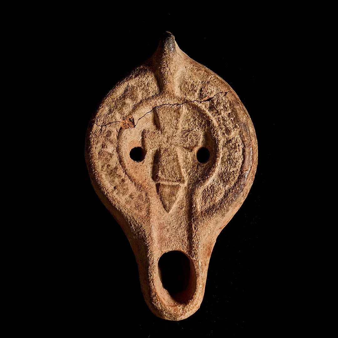 Ancient terracotta artifact with cross, two circular holes for air, on a black background.