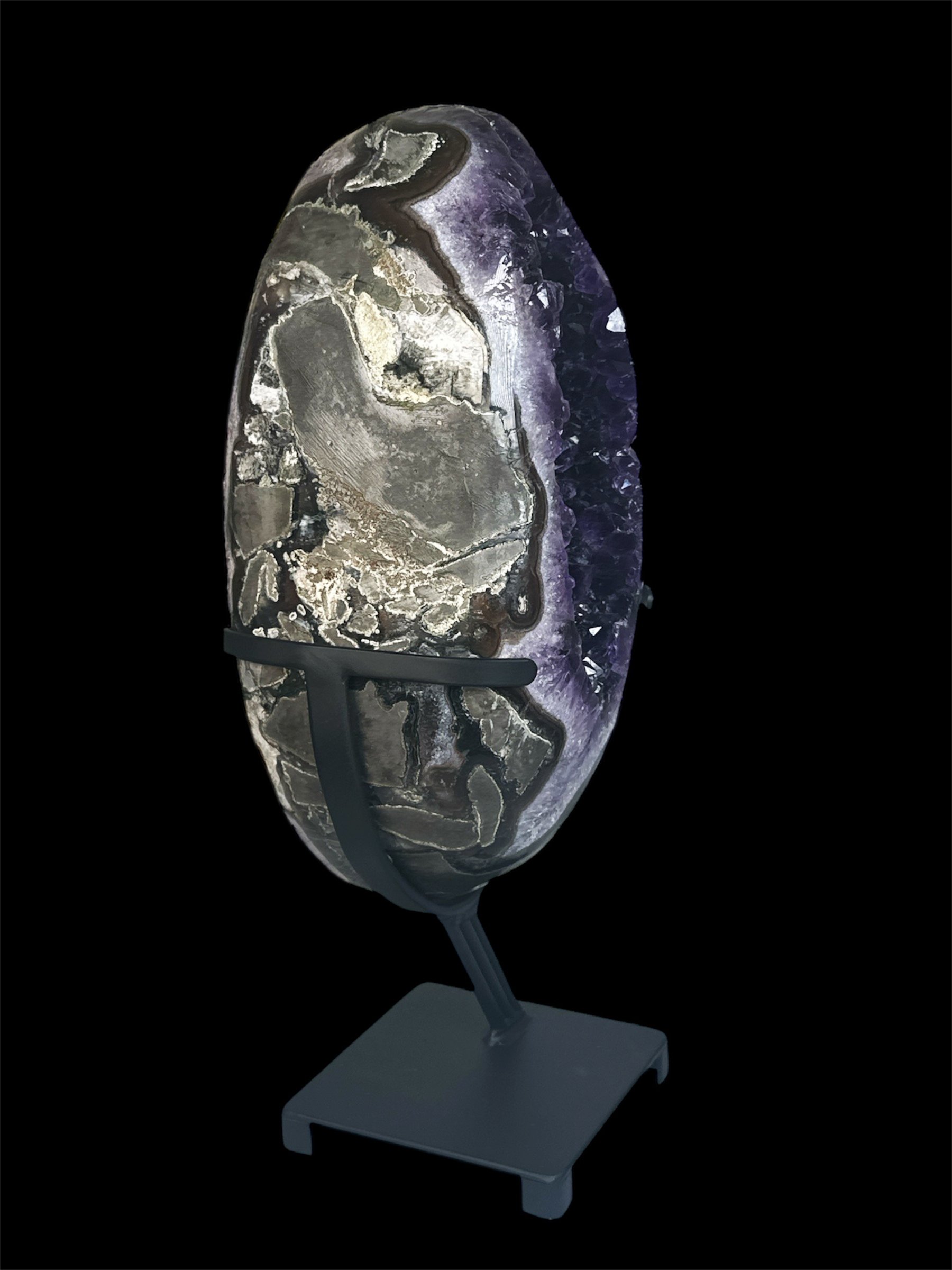 Large polished stone or geode with purple, gray, and white layers on a black background, mounted on a black stand.